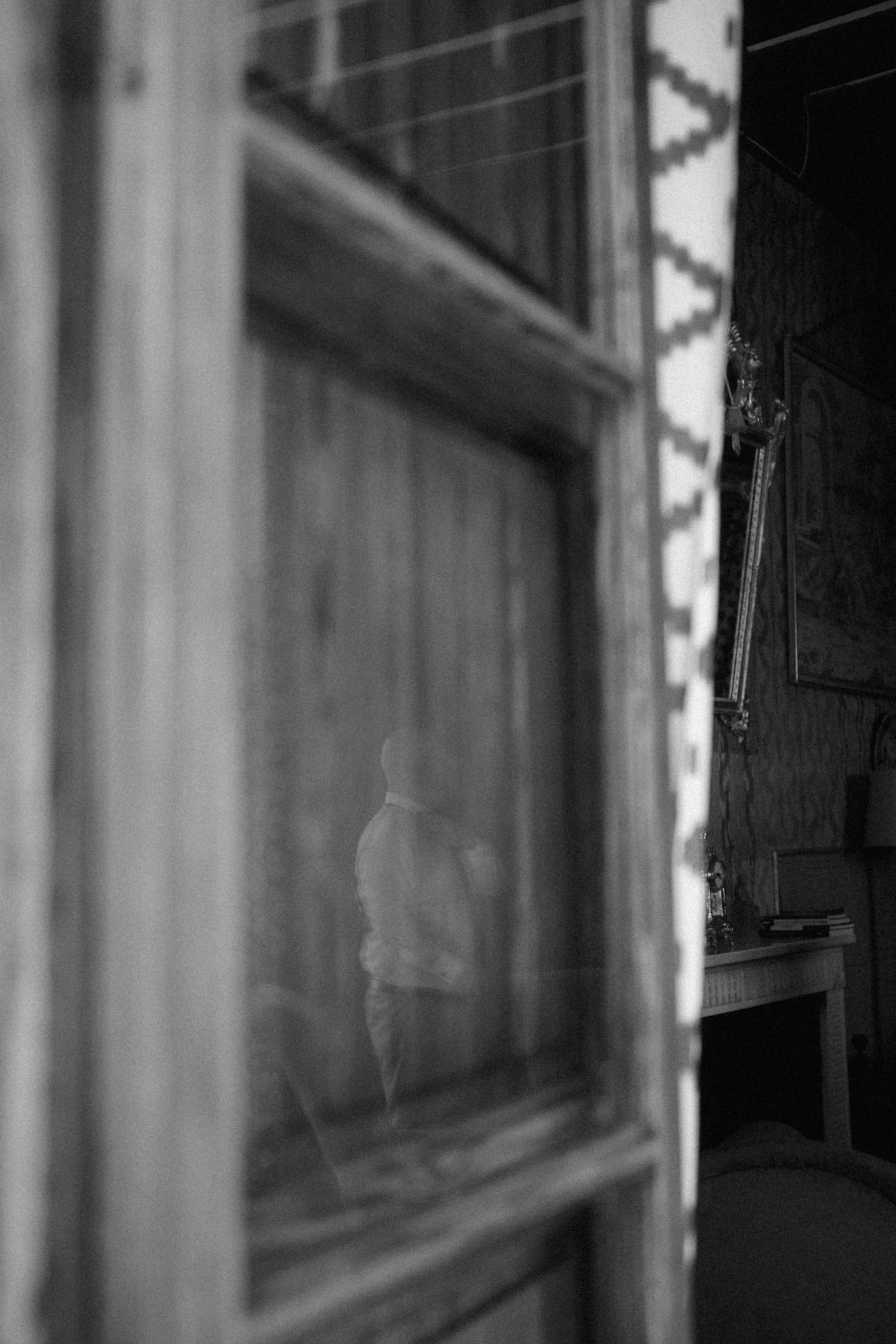 Black and white photo of a figure reflected through an old wooden window frame.
