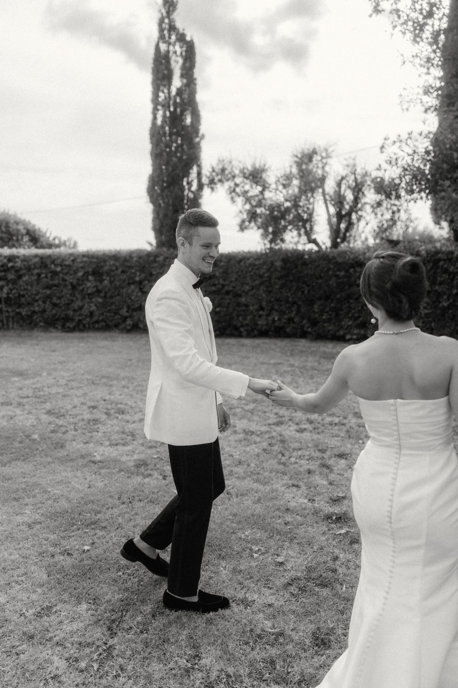 Black and white photo of a groom in white tuxedo dancing with bride in strapless gown outdoors.