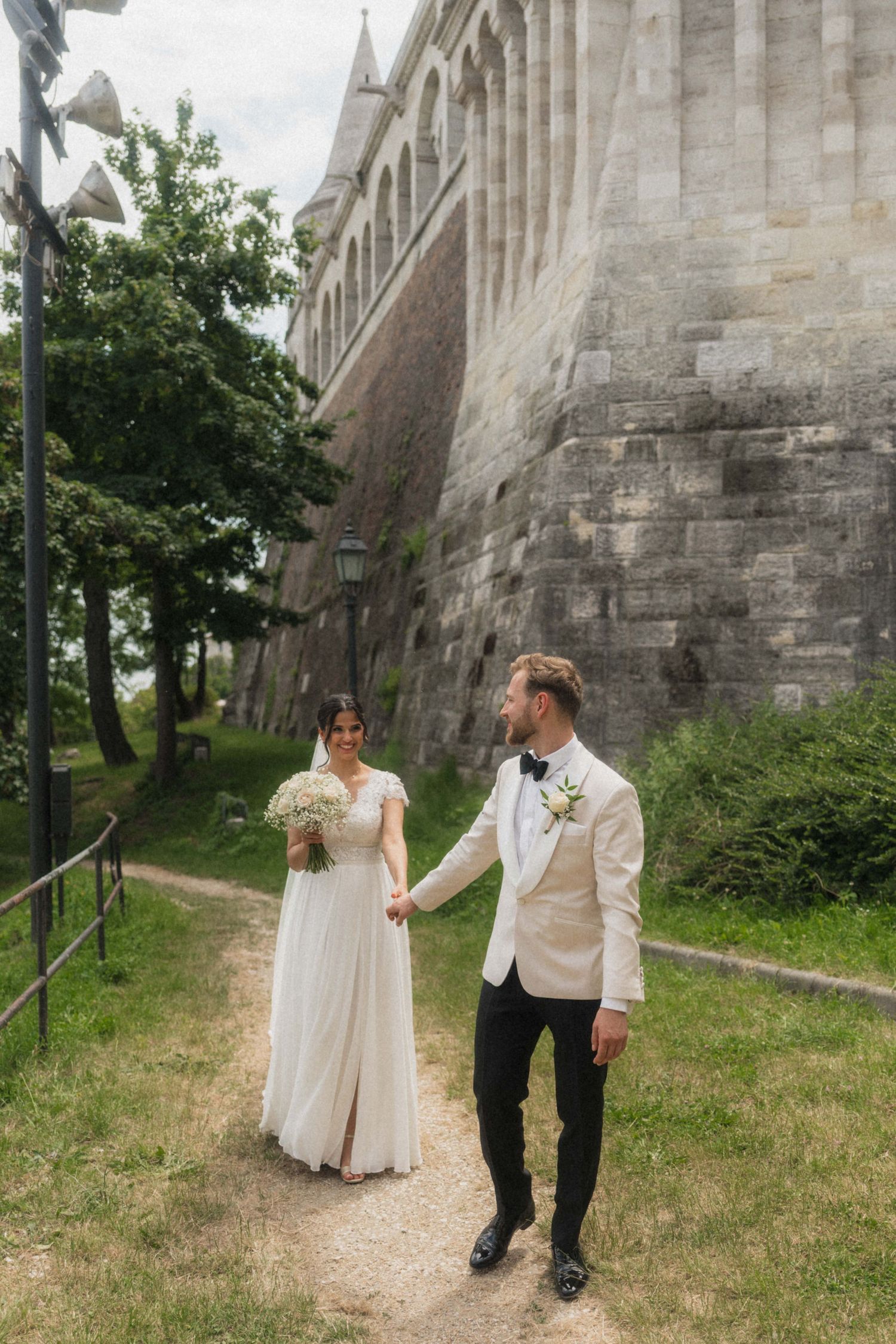 Bride and groom holding hands walking along a stone castle path on their wedding day.