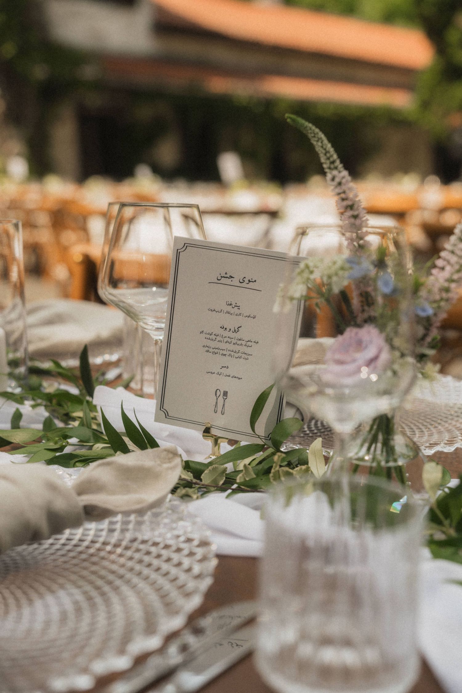 Elegant outdoor wedding table setting with greenery runner, menu card, and floral centerpiece.