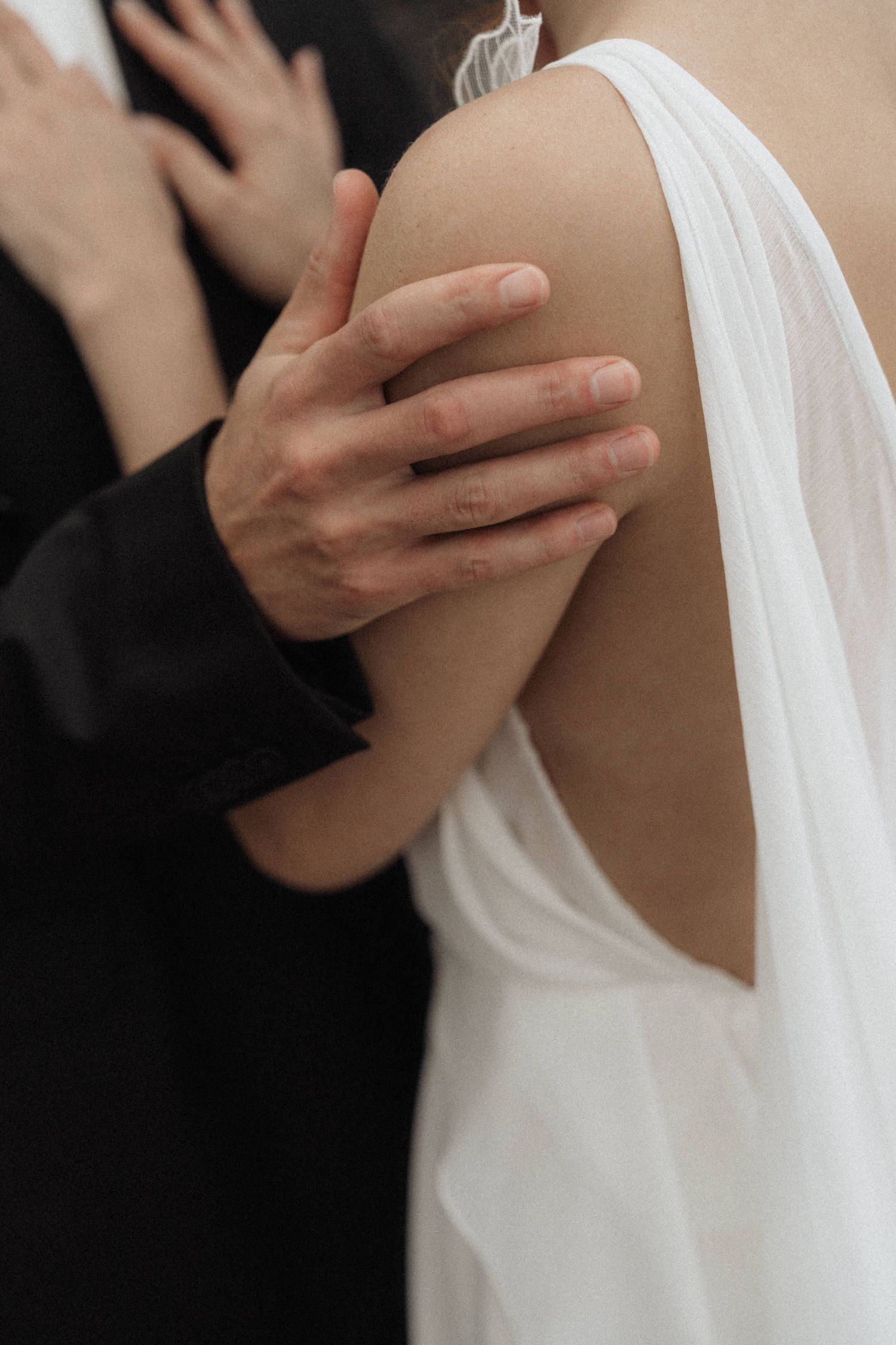 Groom's hand gently resting on bride's bare shoulder in elegant white wedding gown.