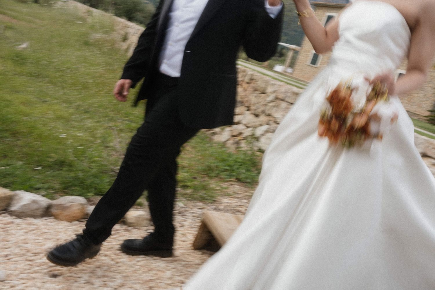 Bride in white gown and groom in black suit walking together outdoors on a wedding day.