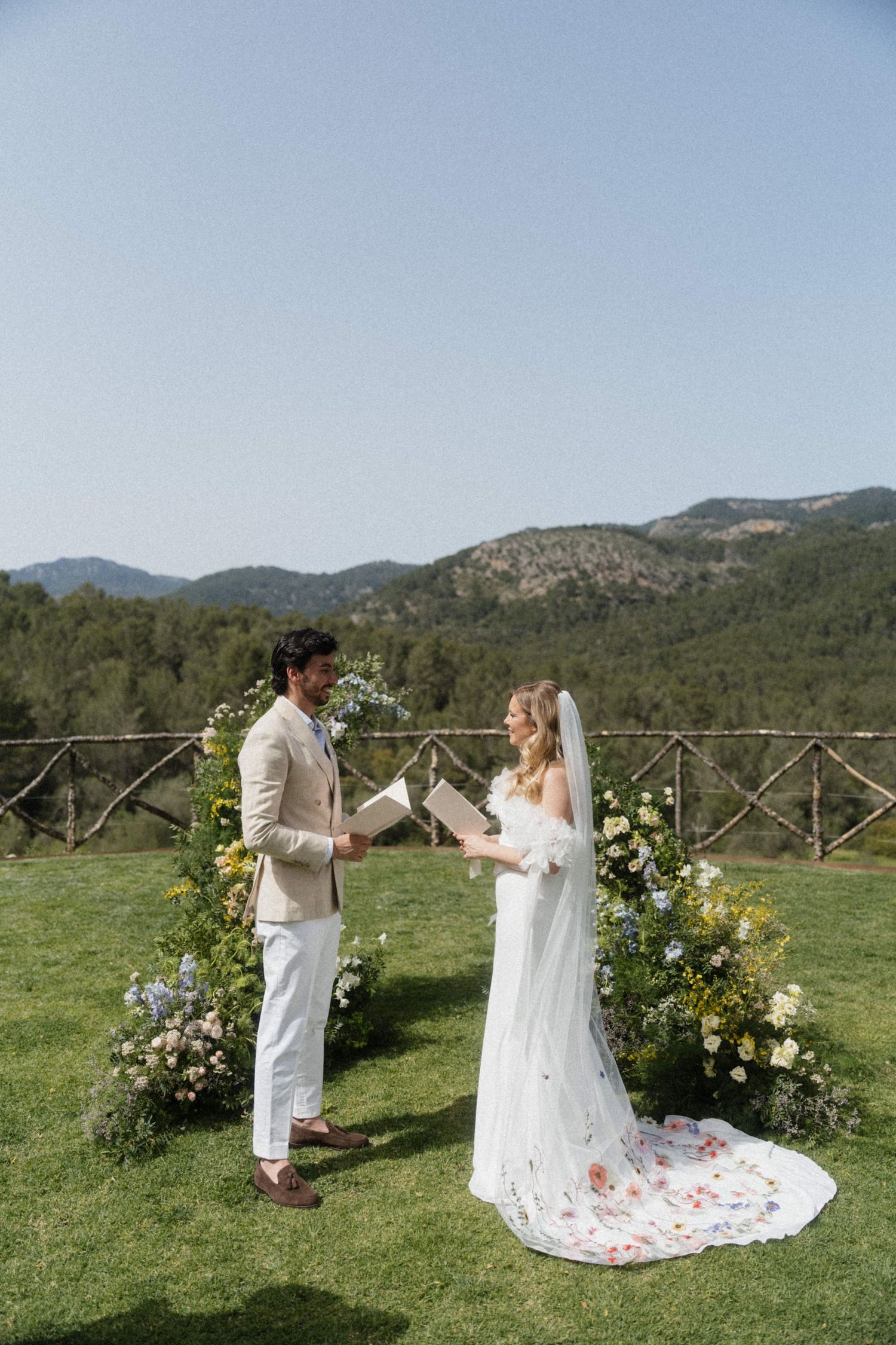 Bride and groom exchanging vows at an outdoor wedding ceremony with floral arch and mountain backdrop.