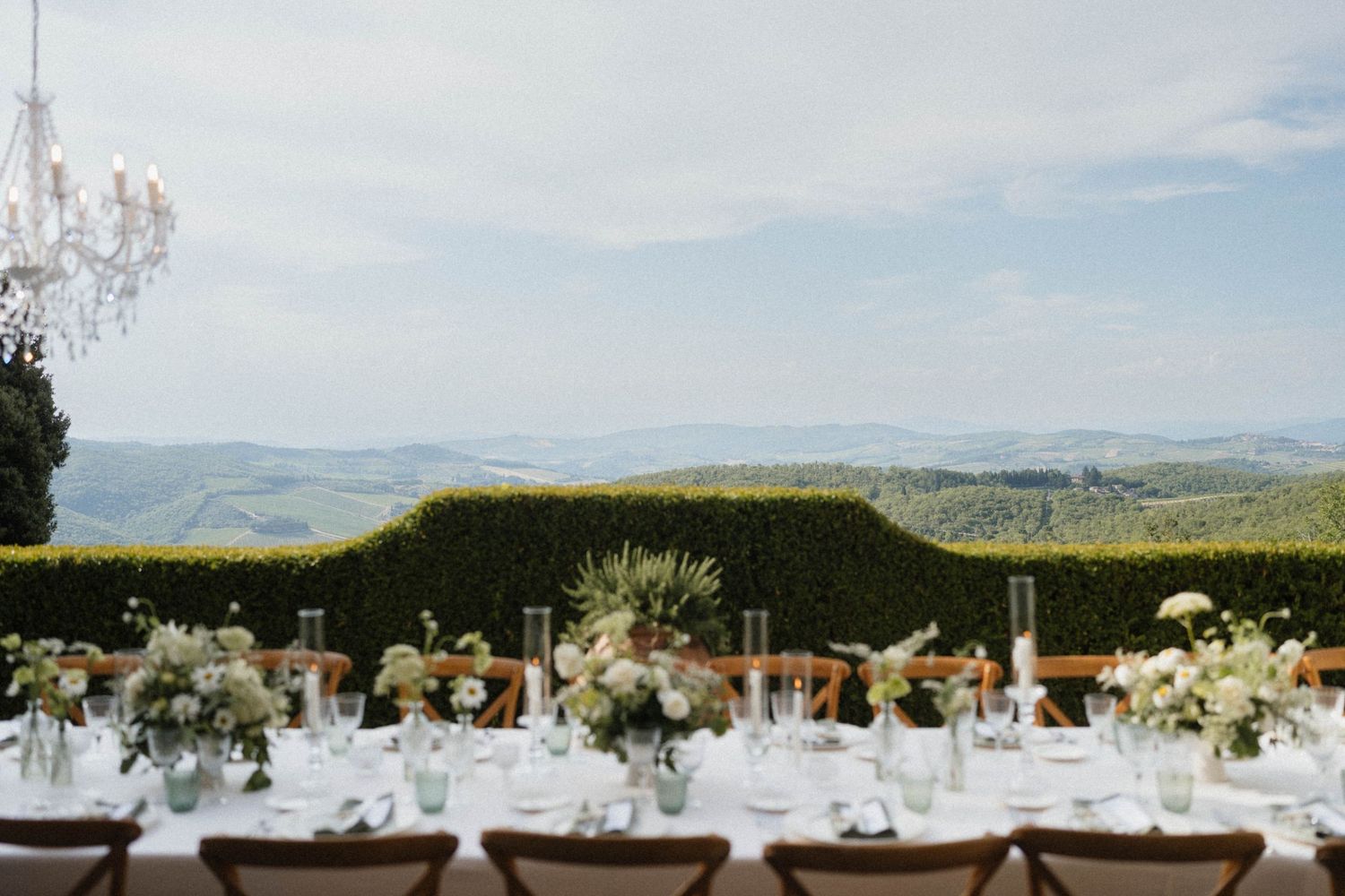 Elegant outdoor wedding reception table with white floral centerpieces overlooking a scenic Tuscan countryside landscape.