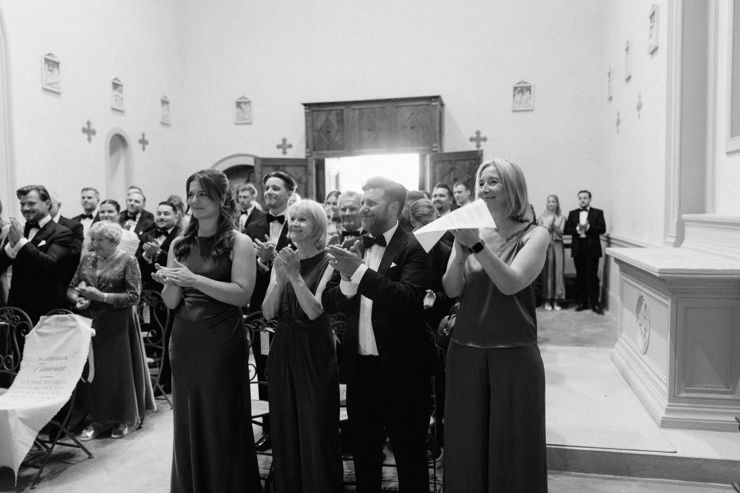 Wedding guests in formal attire applaud and celebrate inside elegant church ceremony.