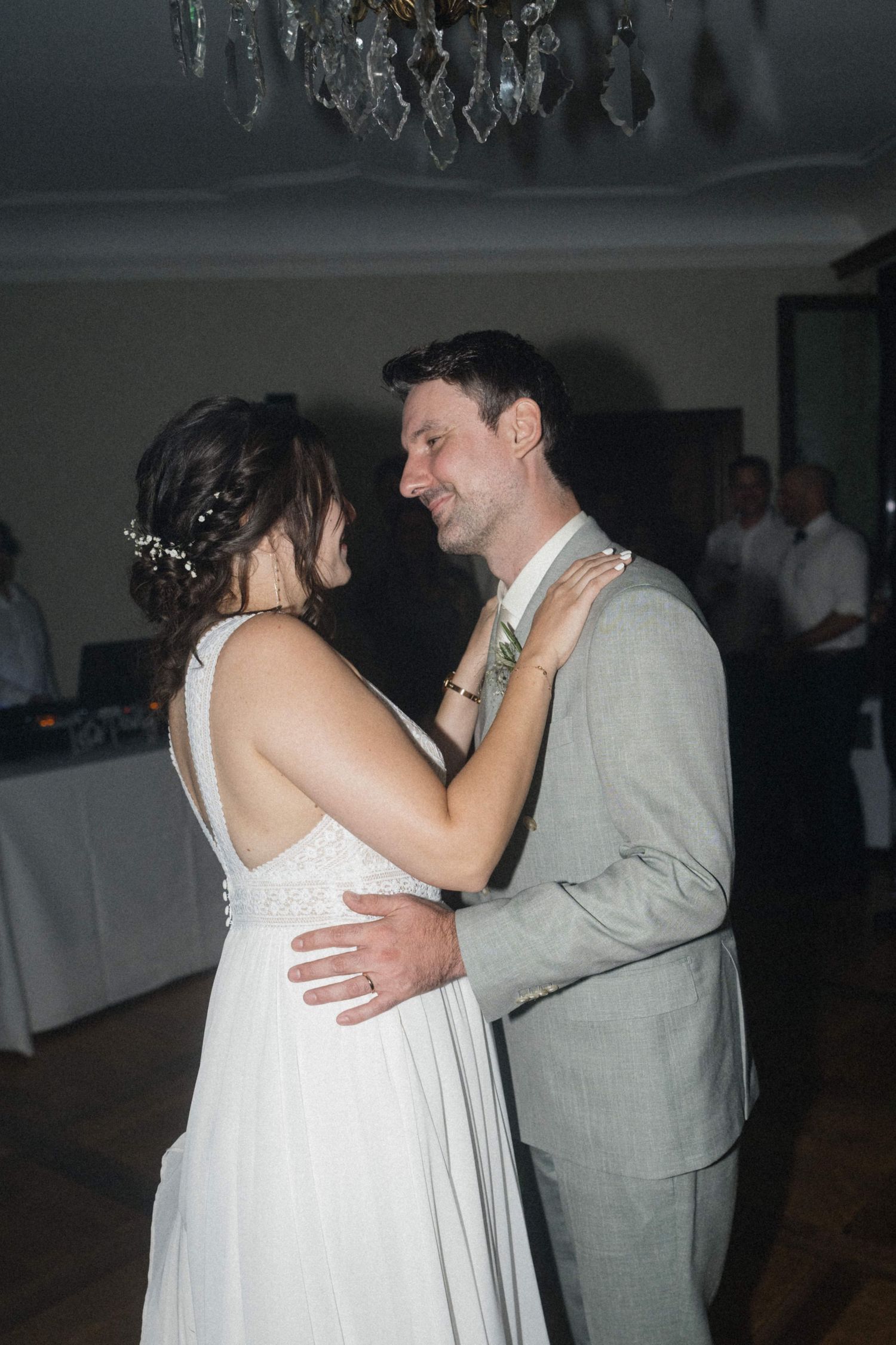Bride and groom share romantic first dance under crystal chandelier at elegant wedding reception.