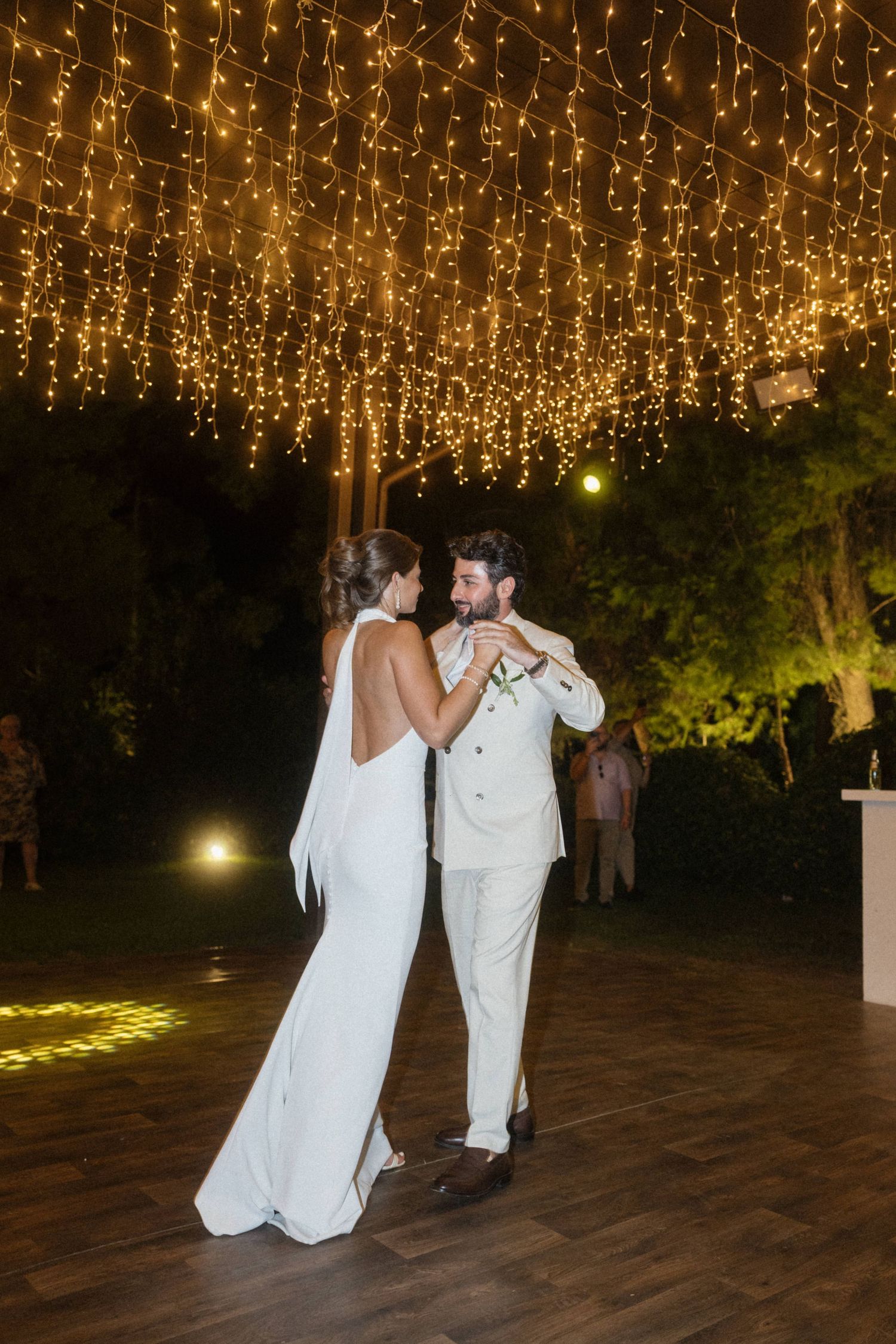 Bride and groom share their first dance under a canopy of warm fairy lights at an outdoor wedding reception.