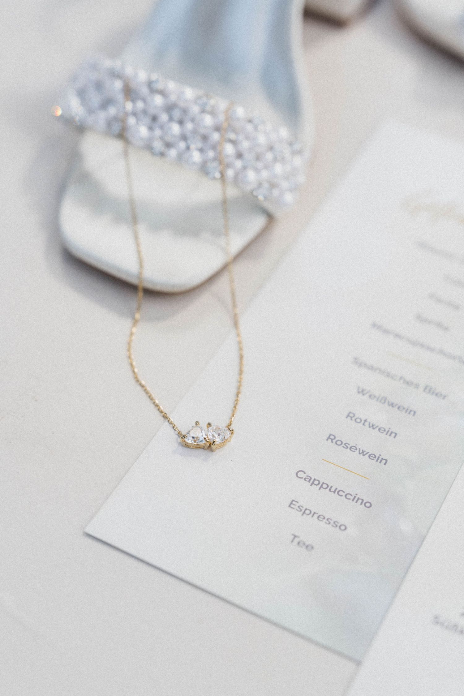 Close-up of a delicate gold crown necklace resting on a wedding menu beside pearl-embellished bridal heels.