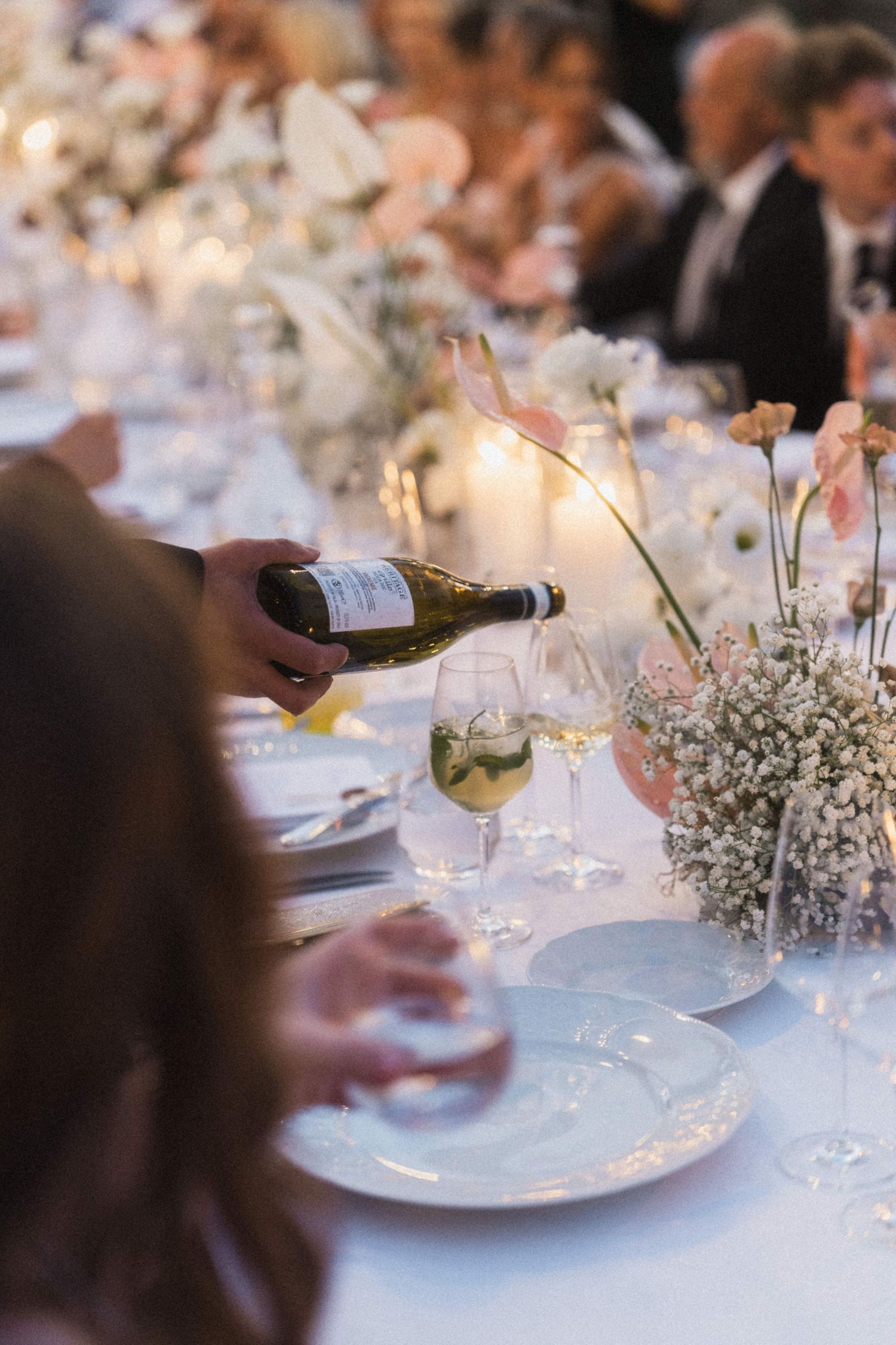 Wine being poured into a glass at an elegant floral wedding reception table.
