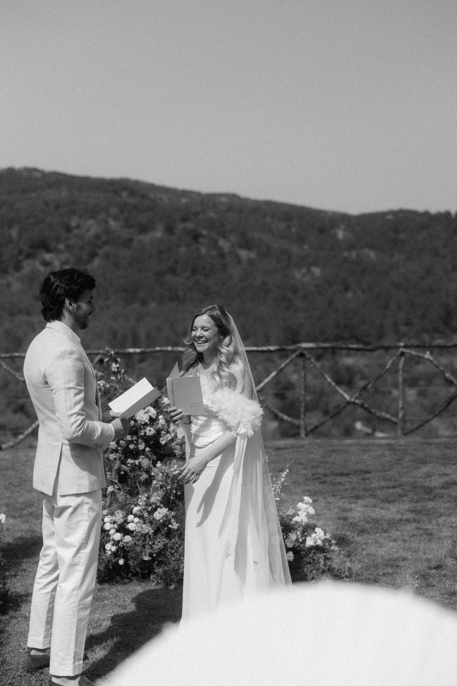 Black and white photo of bride and groom exchanging vows outdoors with mountain backdrop.