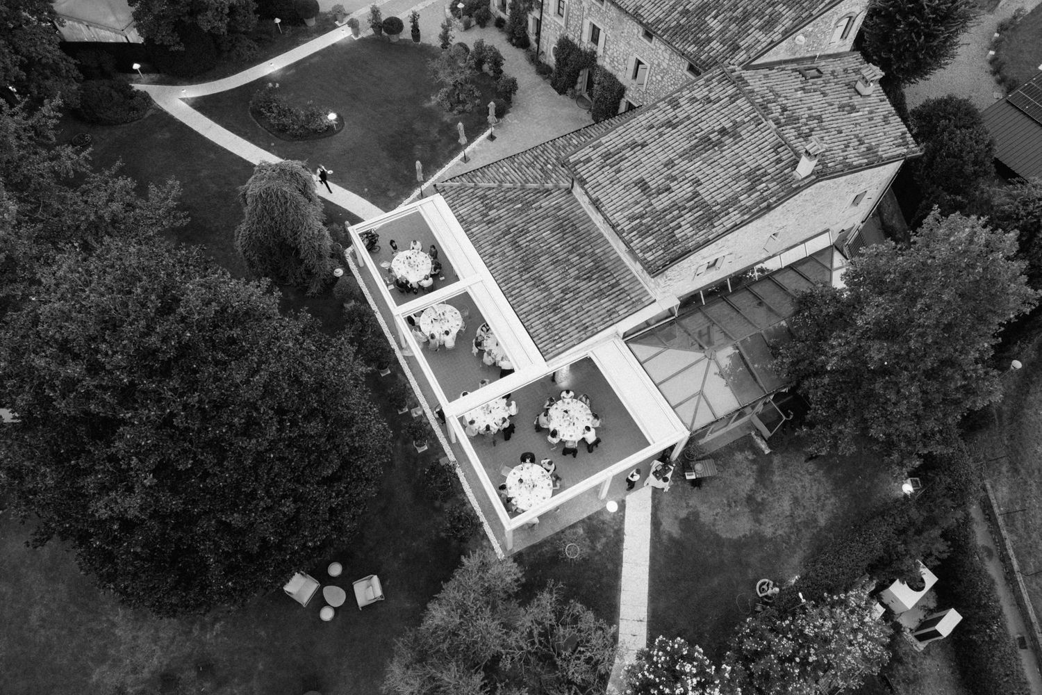 Aerial black and white view of a historic stone villa with outdoor reception tables set in a lush garden.