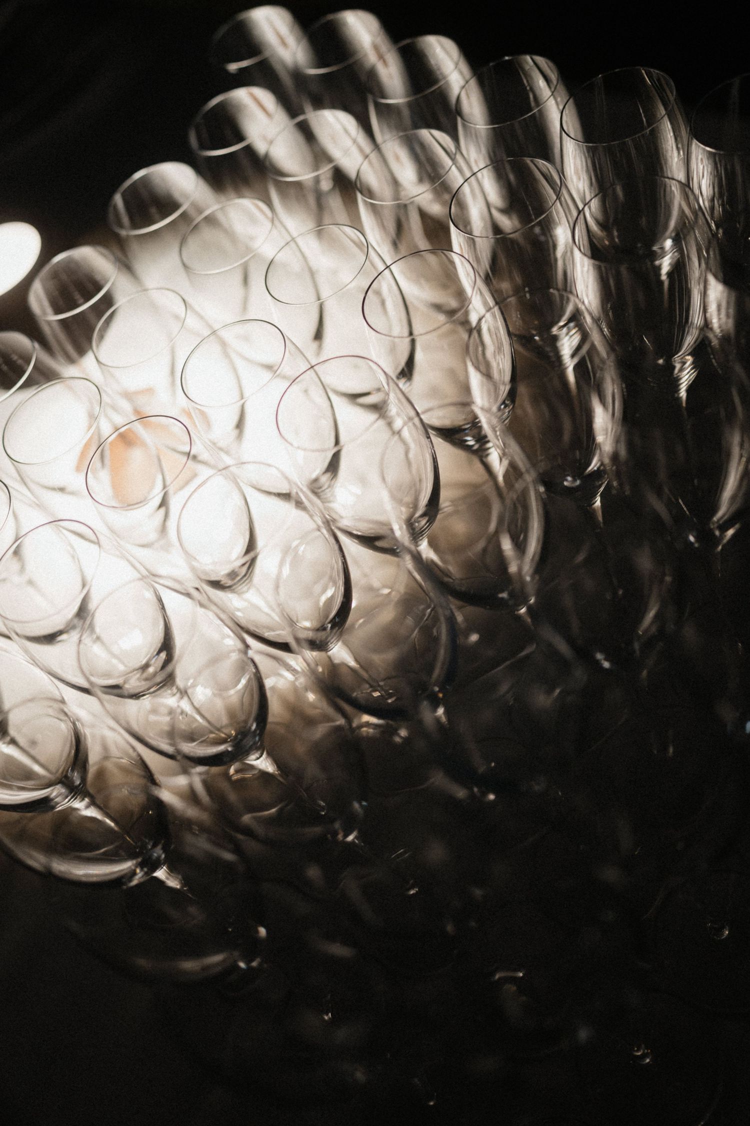 Artistic overhead view of rows of elegant empty champagne flutes arranged in a pattern under dramatic lighting on dark background.