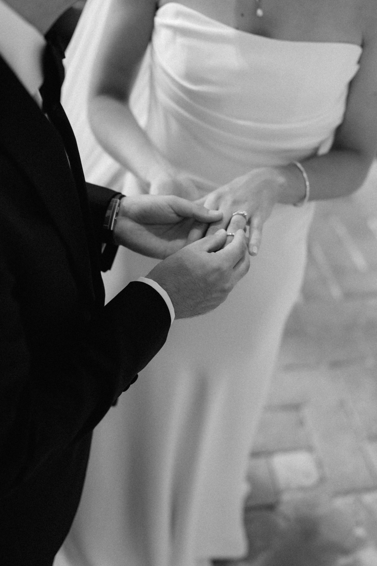 Black and white photo of groom placing wedding ring on bride's finger during ceremony.