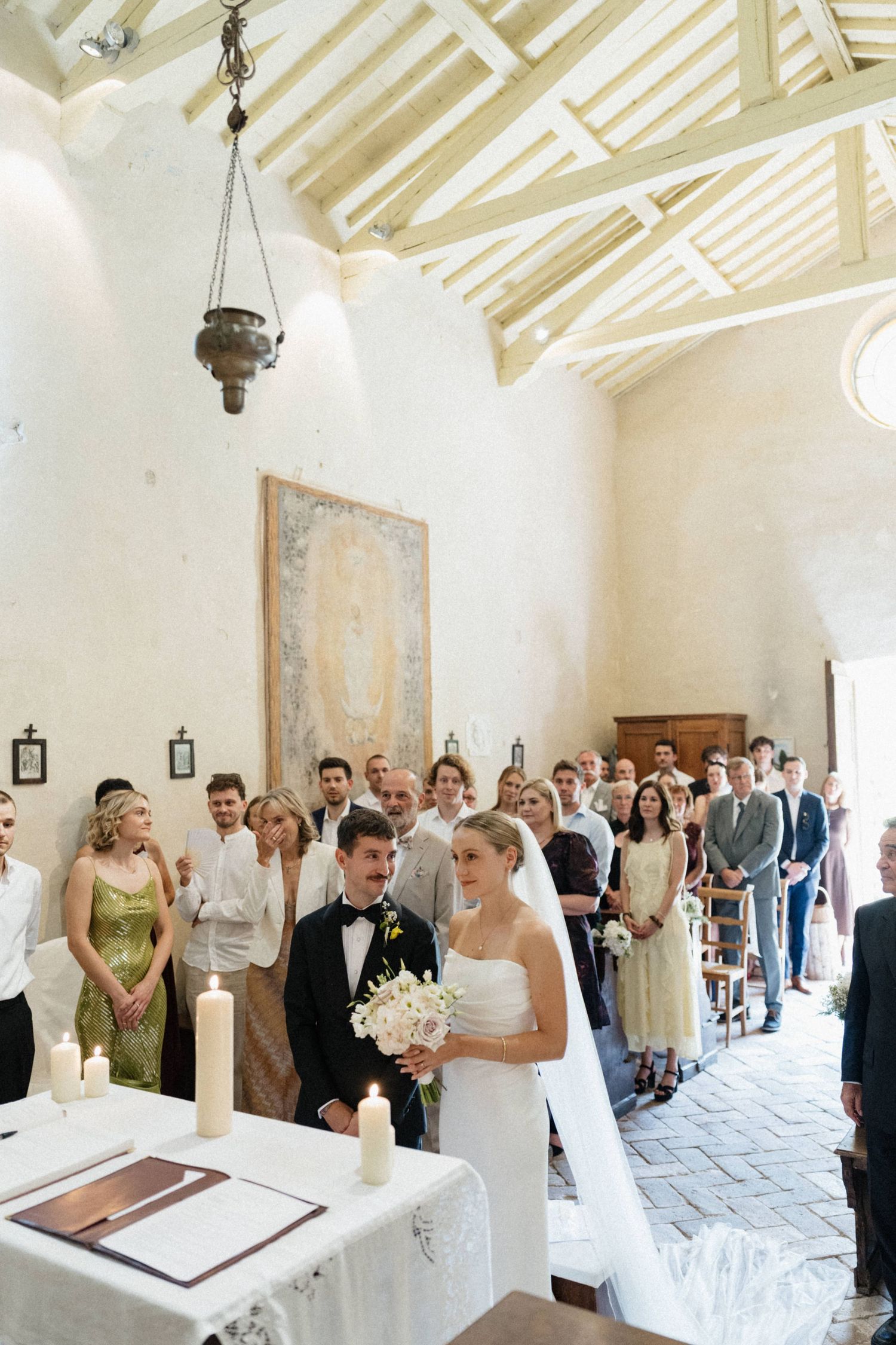 Bride and groom stand at the altar of a rustic chapel with vaulted ceilings and wedding guests.