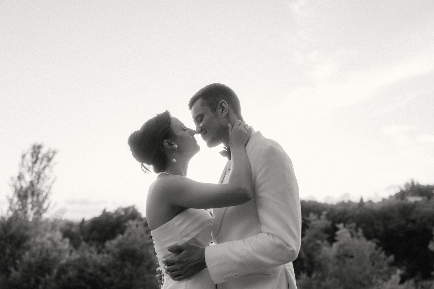 Black and white romantic portrait of bride and groom almost kissing at sunset.
