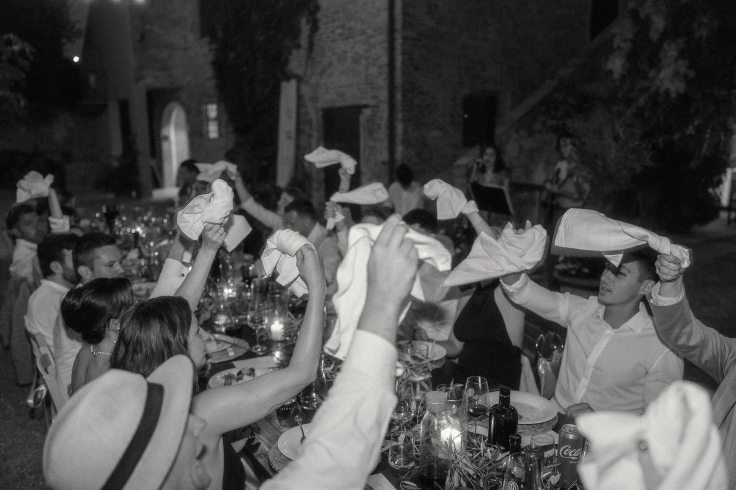 Black and white photo of wedding guests waving napkins in lively celebration at night.