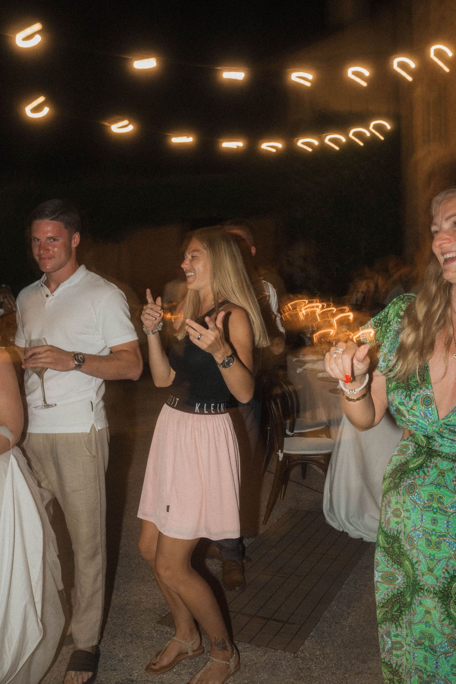 Wedding guests dancing under string lights at outdoor evening reception celebration.