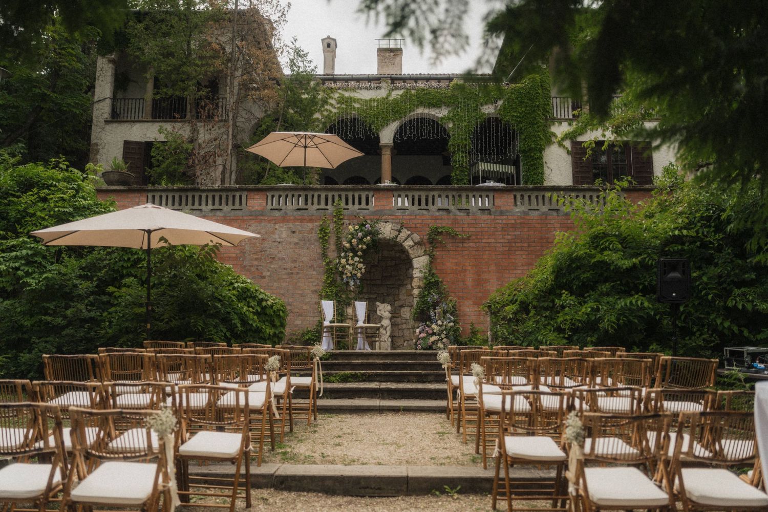 Elegant outdoor wedding ceremony setup with wooden chairs at a rustic Italian villa surrounded by lush greenery.