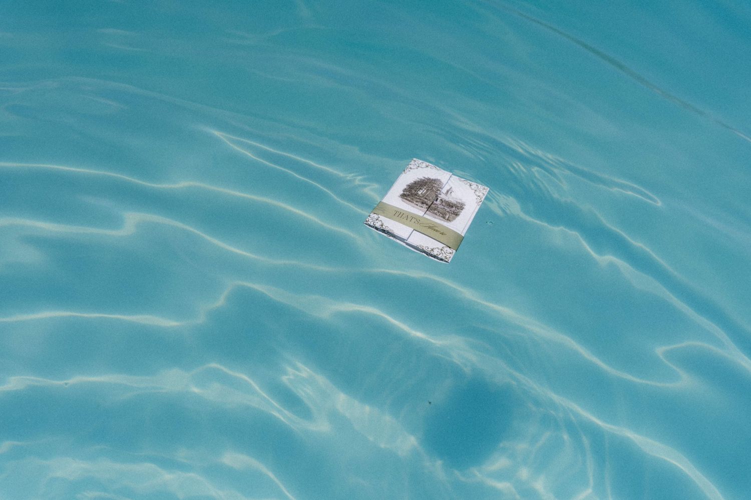 A small photograph floating on the surface of clear turquoise water in a pool.