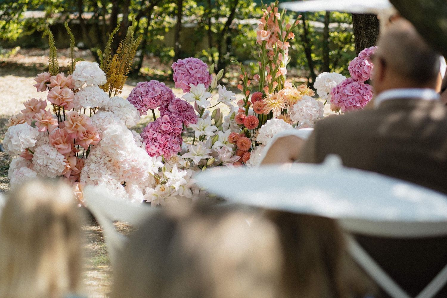 Lush pink and white floral arrangements line the aisle at an elegant outdoor wedding ceremony.