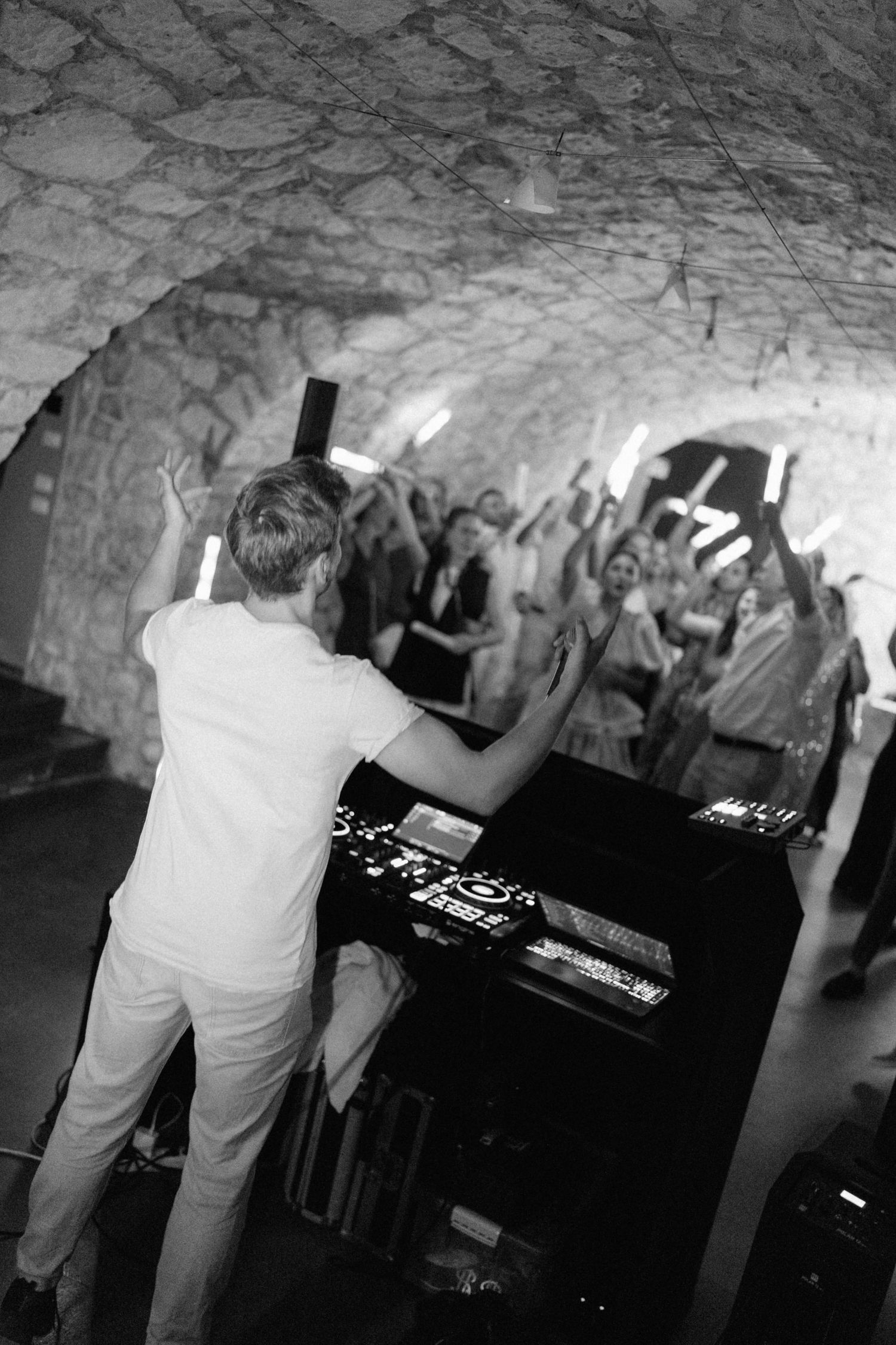 Black and white photo of a DJ performing for a crowd in a stone cave venue.