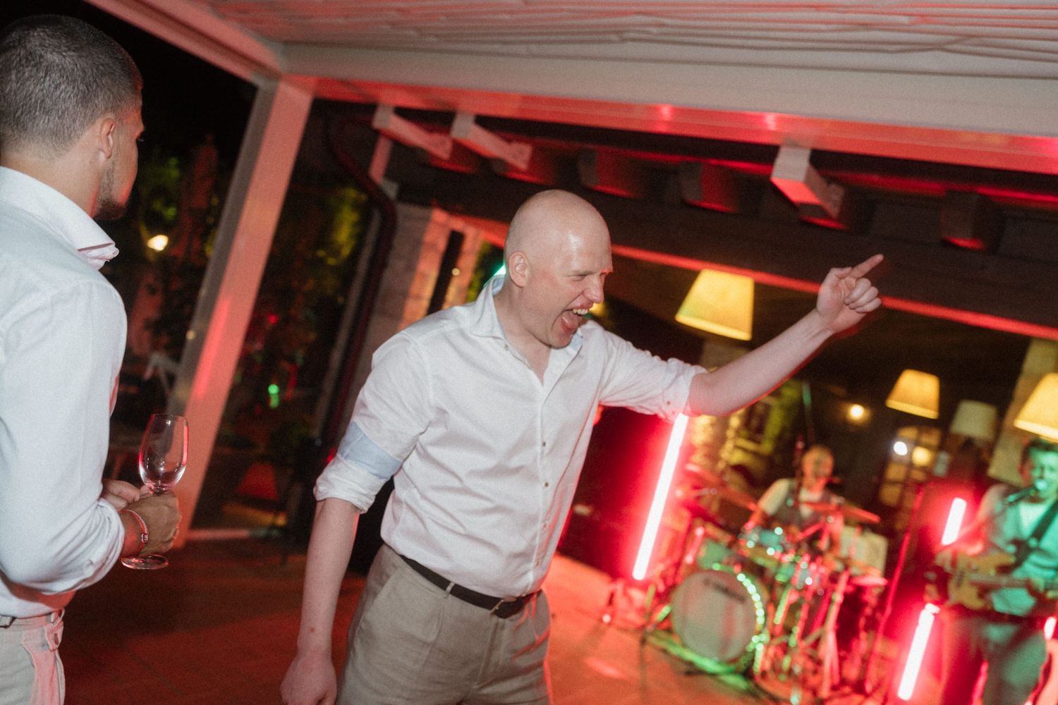 Bald man in white shirt pointing at a red-lit venue during an indoor party or event.