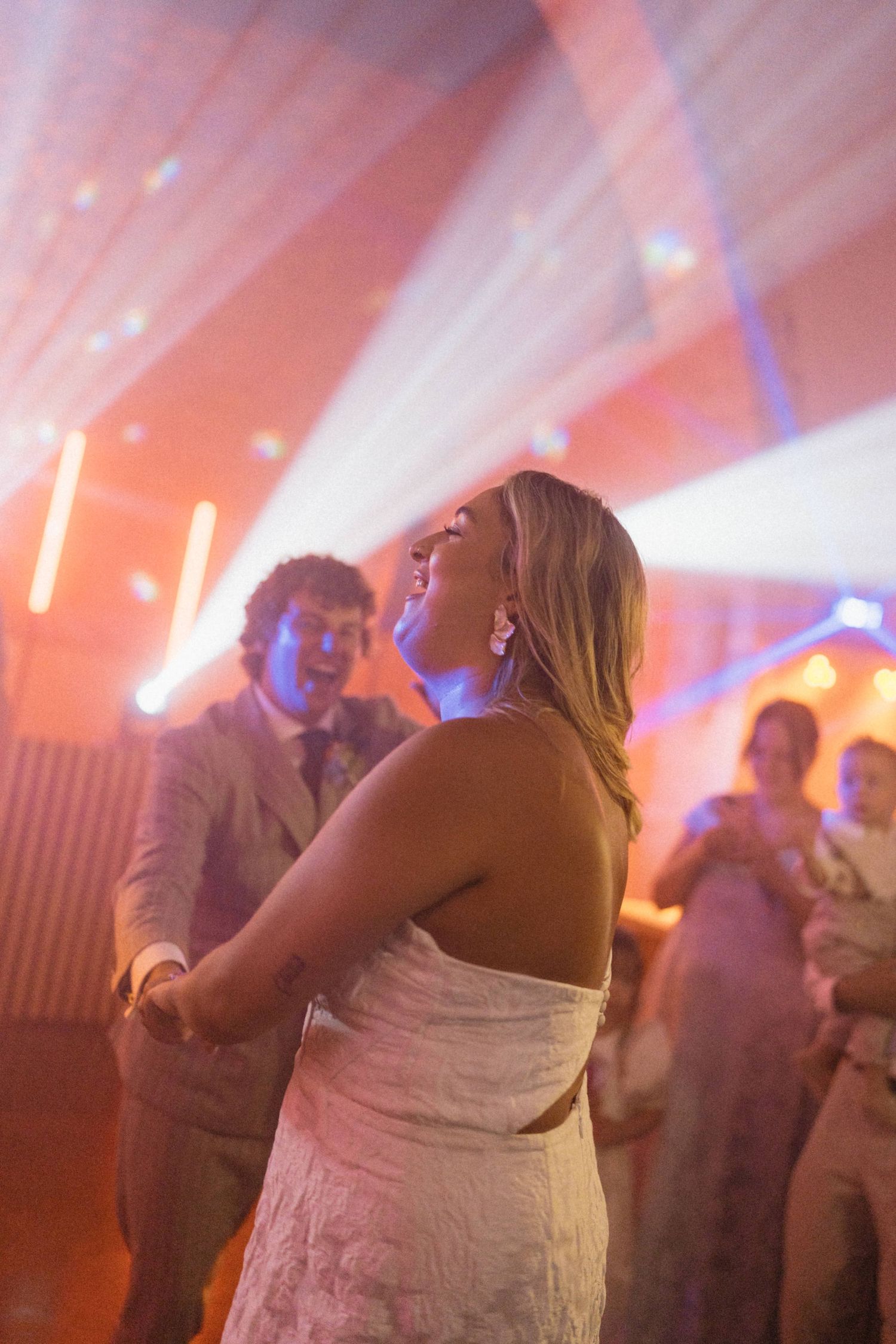 Bride and groom share their first dance under colorful stage lights at a wedding reception.