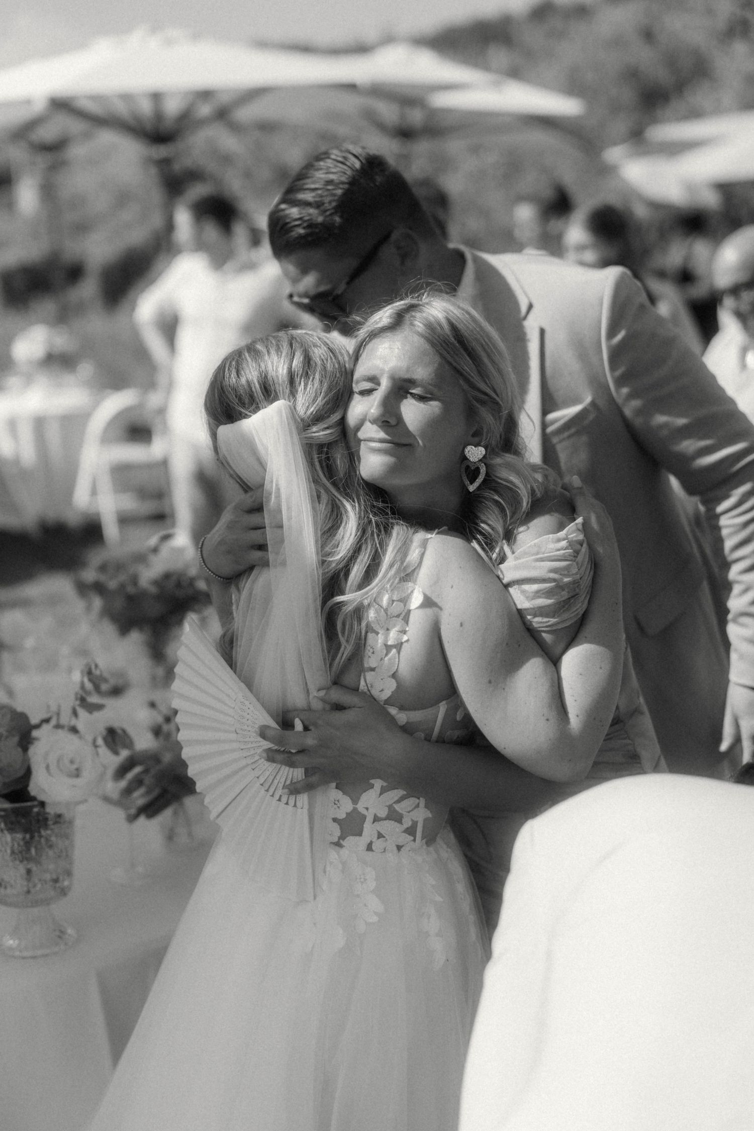 Emotional black and white photo of a smiling bride hugging guests at an outdoor wedding reception.