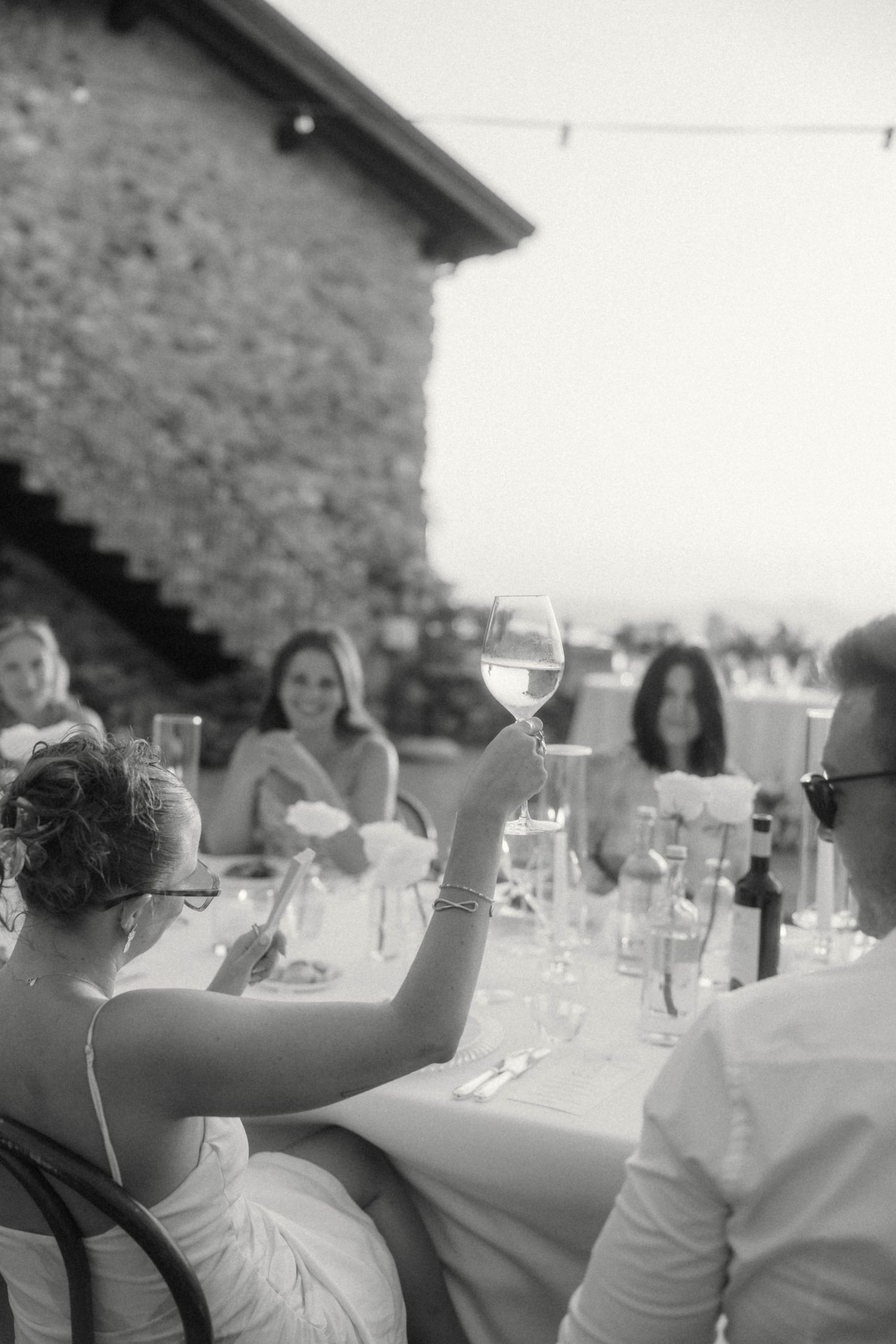 Black and white photo of bride raising wine glass at wedding reception.