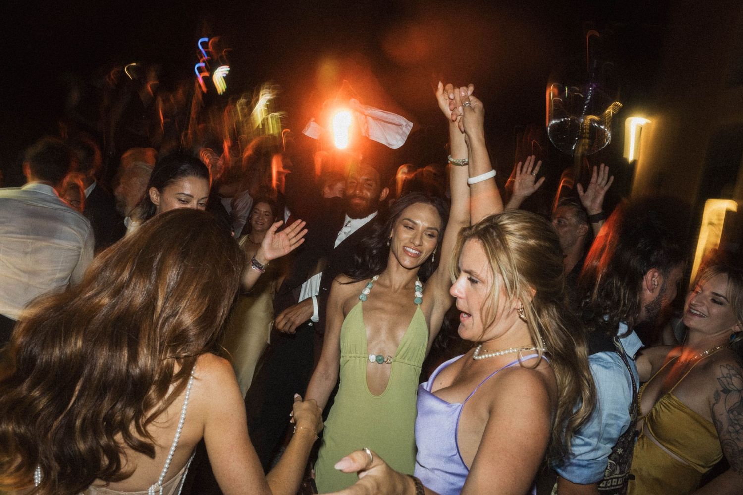 Excited wedding guests dancing and celebrating together at lively outdoor nighttime wedding reception party.