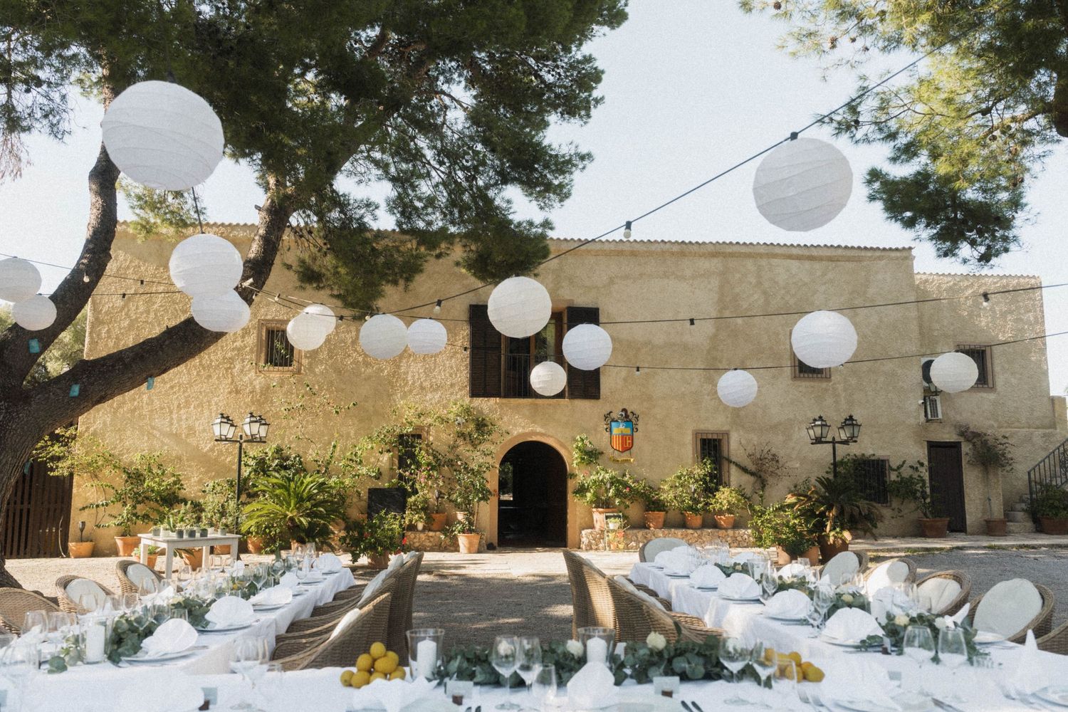 Rustic stone venue decorated with white lanterns and long dining tables for outdoor wedding reception.