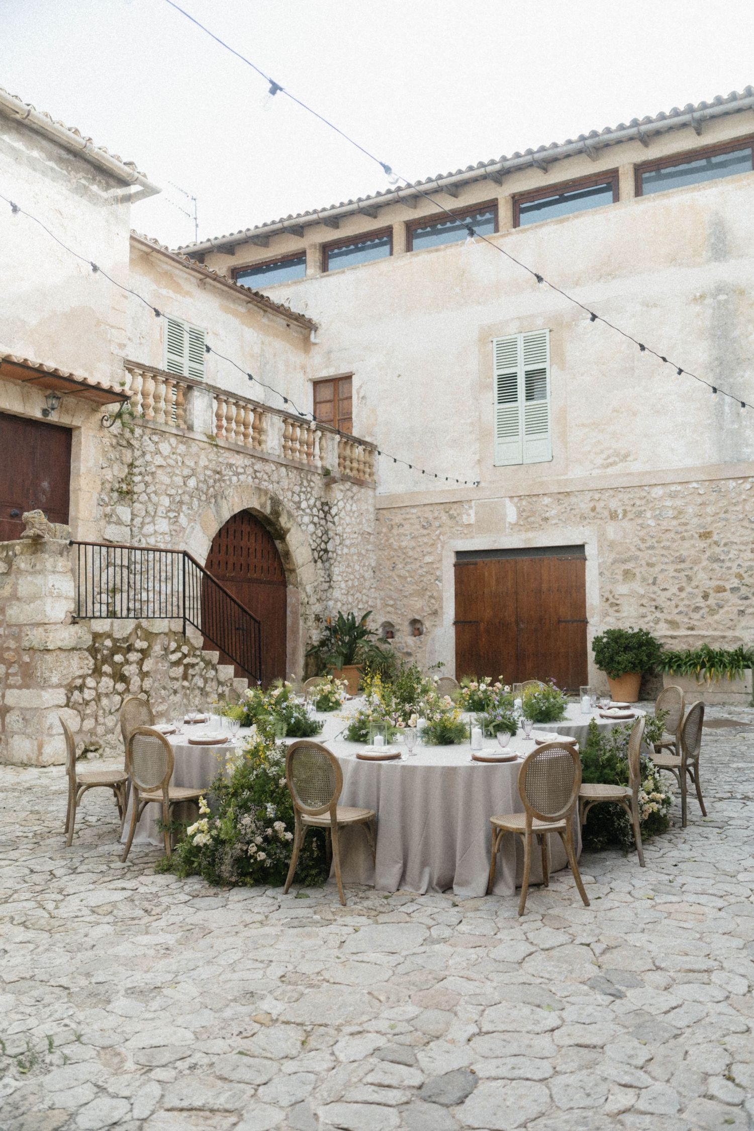 Elegant outdoor wedding reception table set in a rustic stone courtyard with string lights and floral centerpieces.