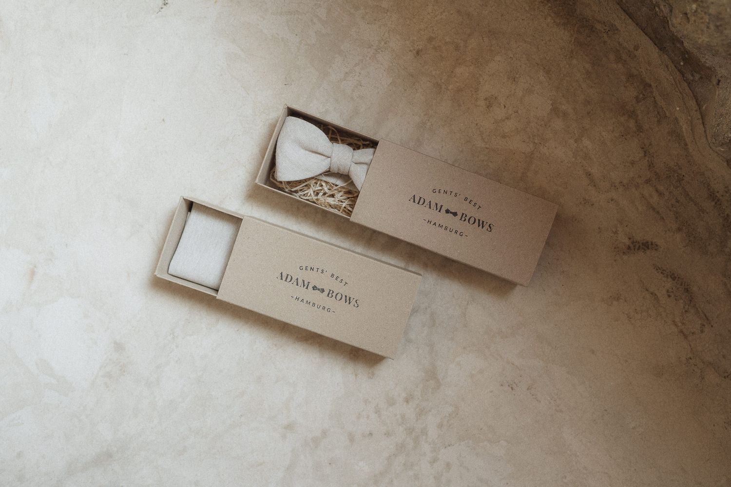 Elegant white bow tie in an open branded gift box on a marble surface.
