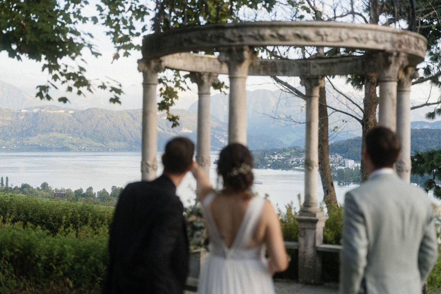 Bride and groom admire scenic lake and mountain views beneath a stone gazebo at their wedding.
