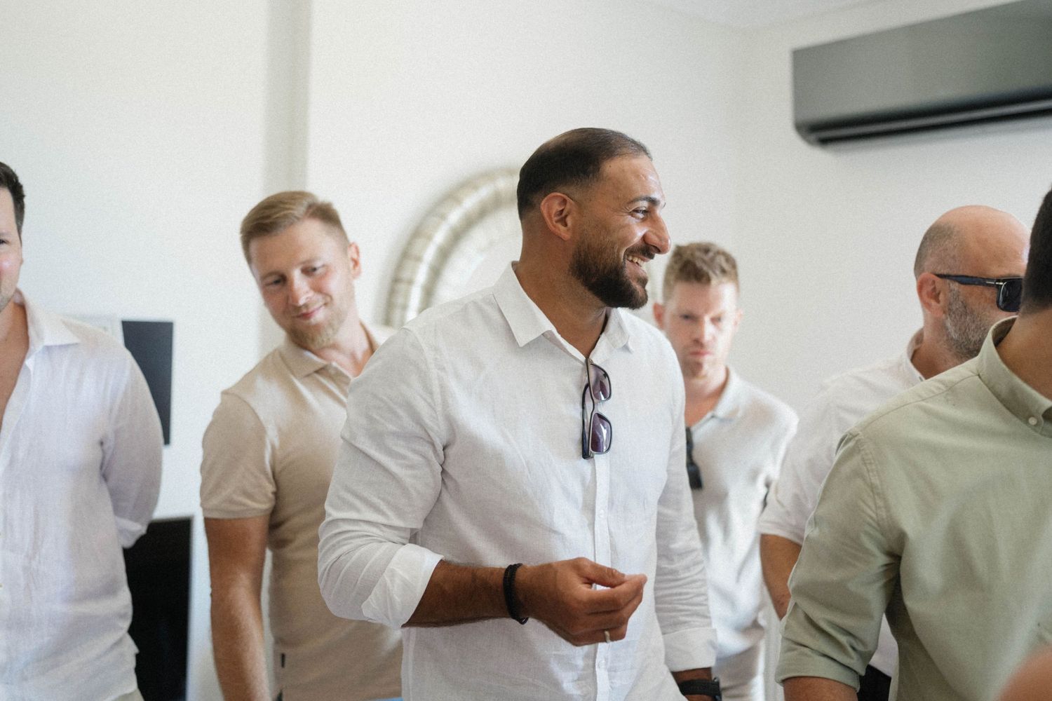 Group of men in white shirts smiling and socializing indoors at a bright, modern venue.