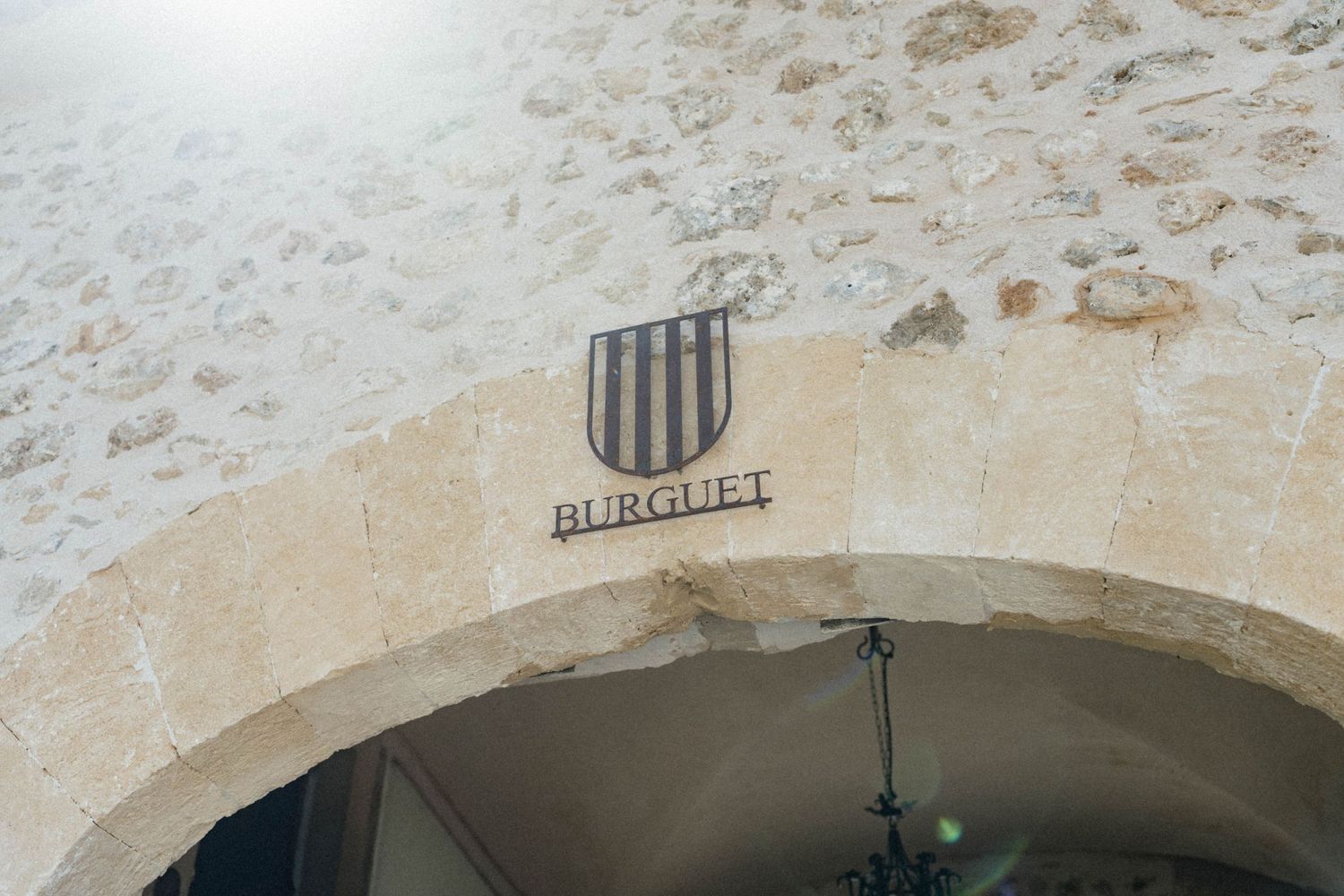 Stone archway entrance with a shield emblem and the name Burgulet engraved above, set in rustic limestone masonry.