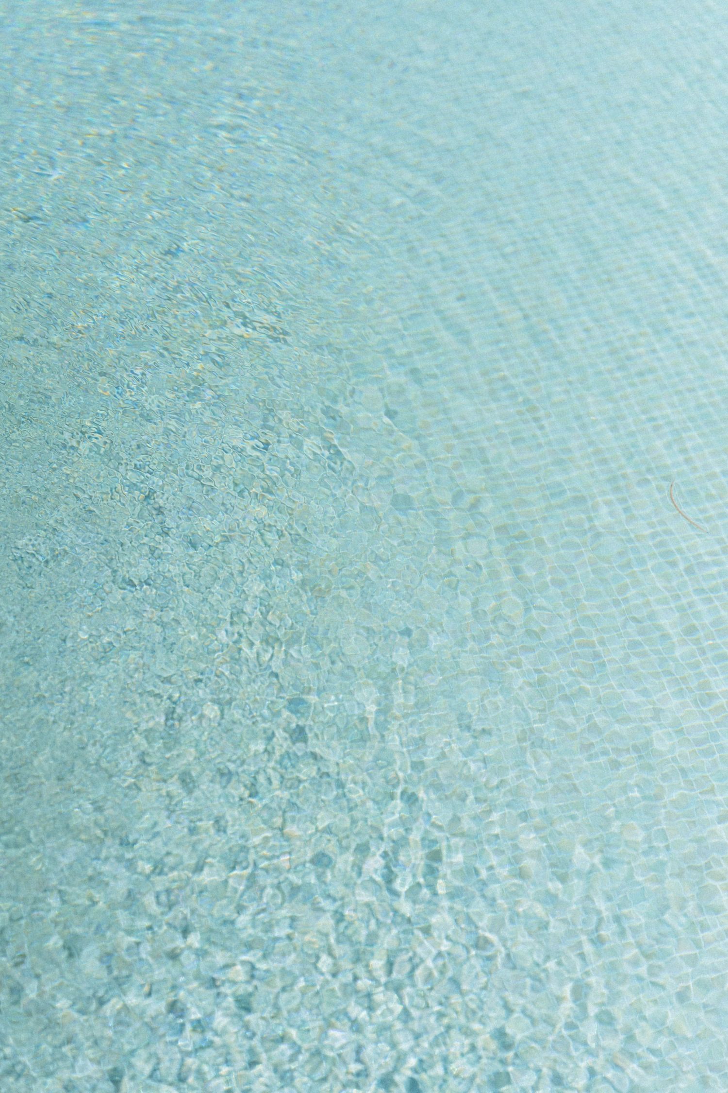 Clear turquoise swimming pool water with rippling light reflections on mosaic tile bottom.