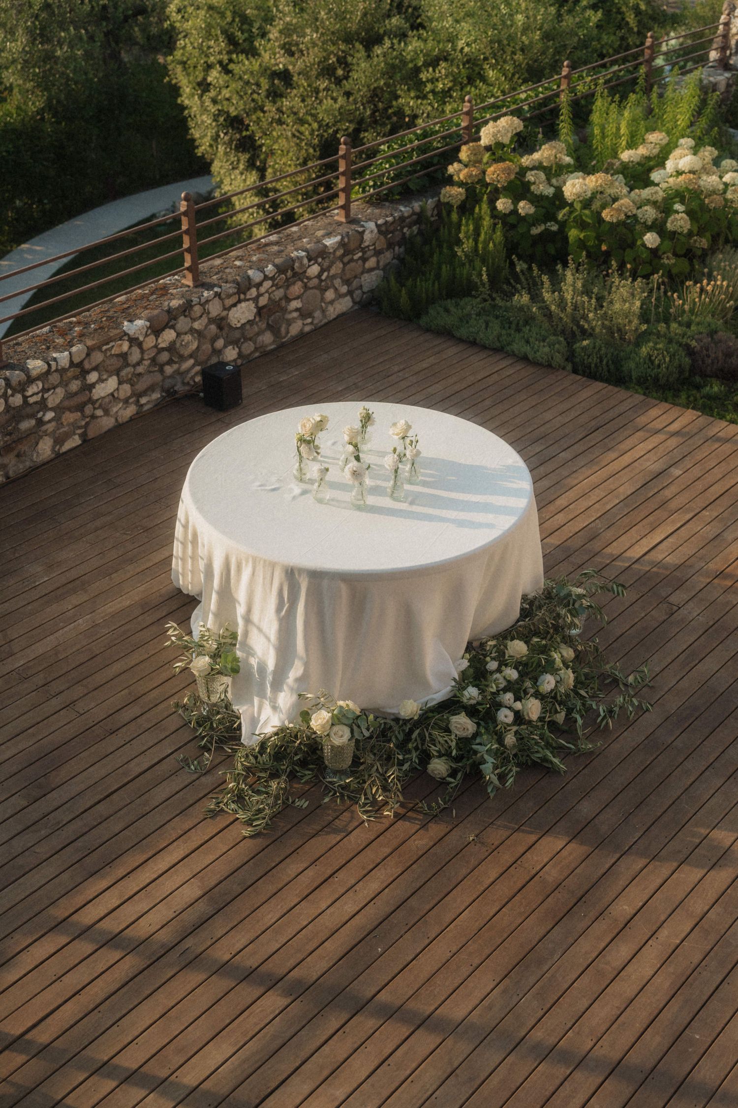 Elegant round wedding table with white linen and floral arrangement on wooden deck outdoor venue.