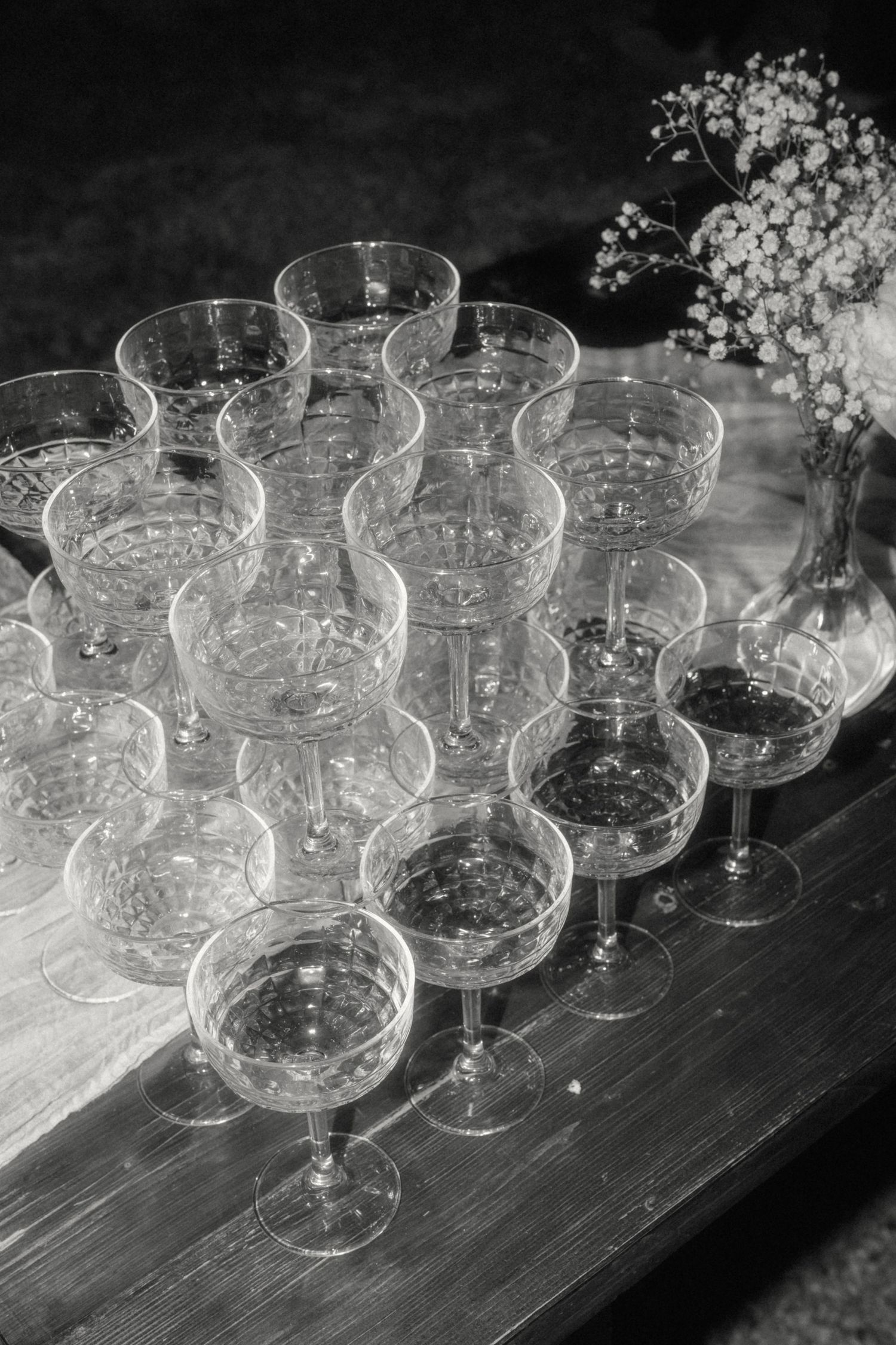 Black and white photo of elegant crystal champagne coupes arranged on a wooden tray with baby's breath.