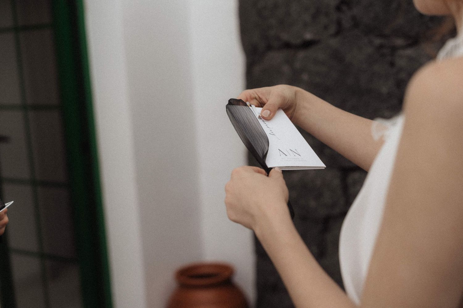 Woman in white dress holding a smartphone and card near a stone wall indoors.