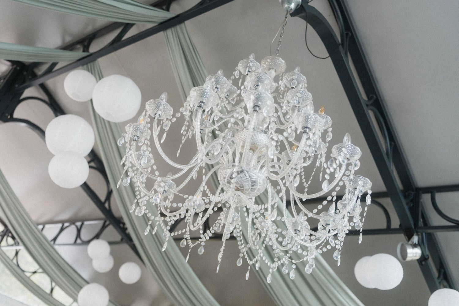 Elegant white crystal chandelier with globe lights hanging in a decorated wedding reception venue.