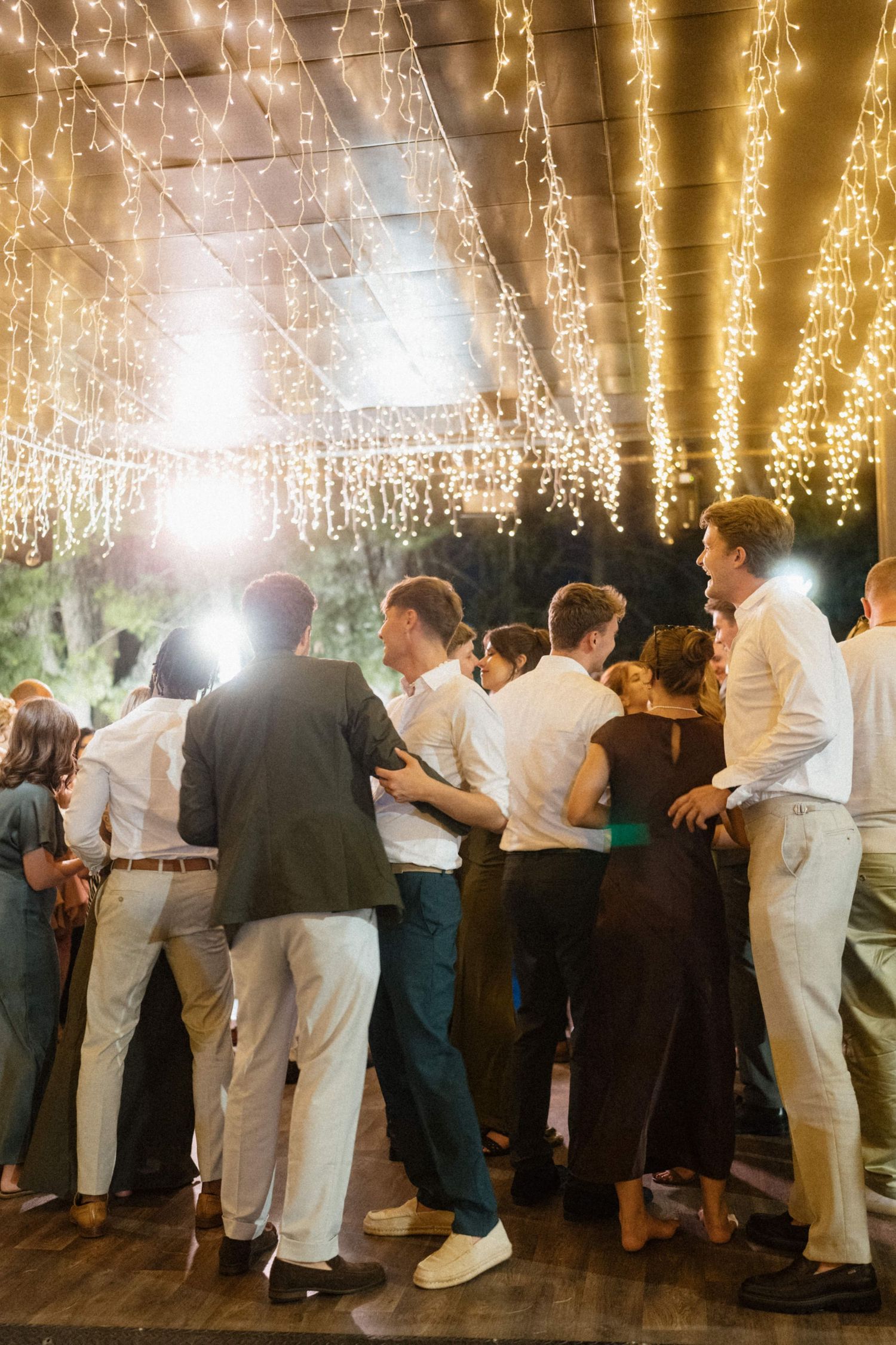 Guests dancing under warm string lights at an elegant indoor evening wedding reception party.