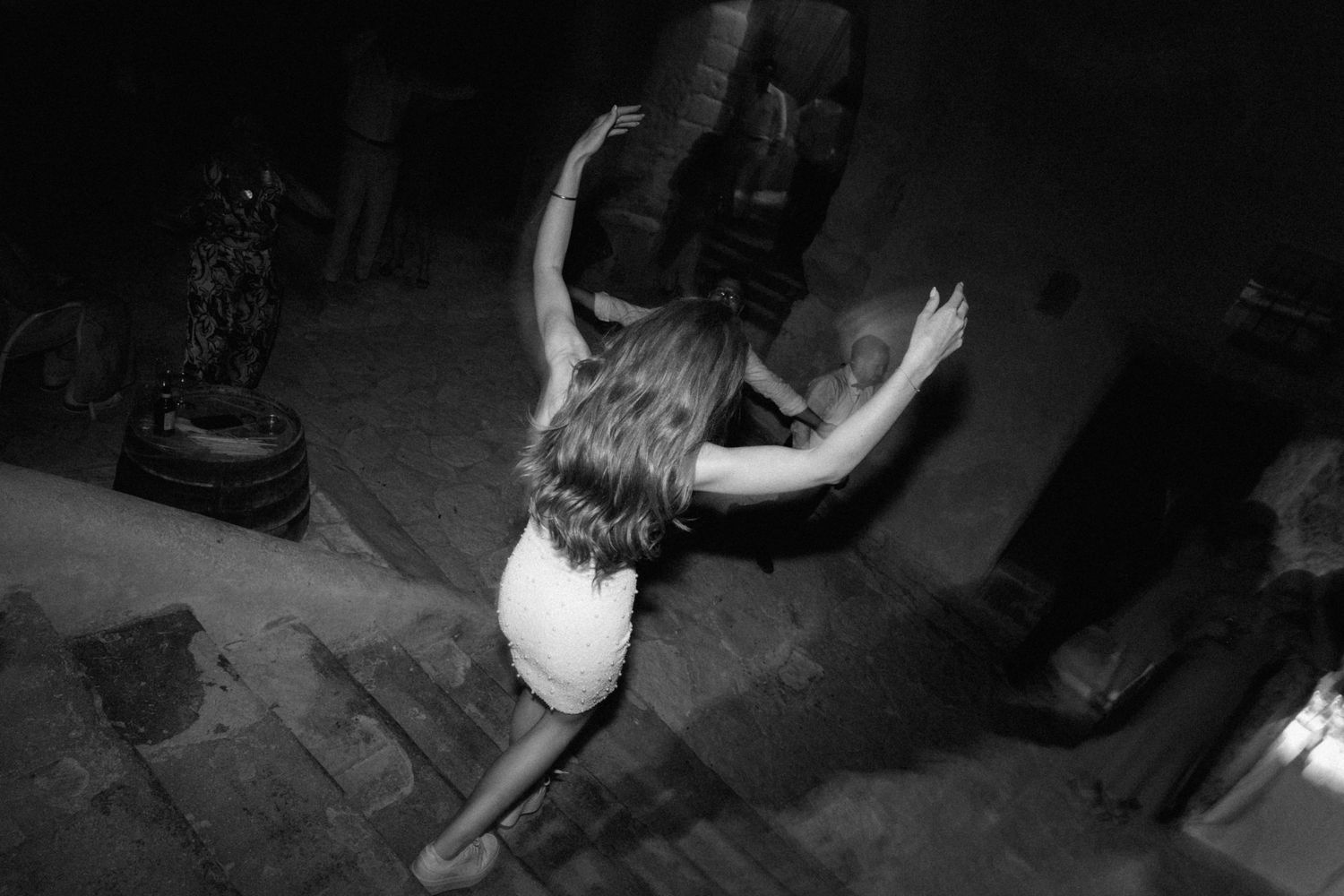 Black and white aerial view of a woman in a white dress dancing at a nighttime party event.