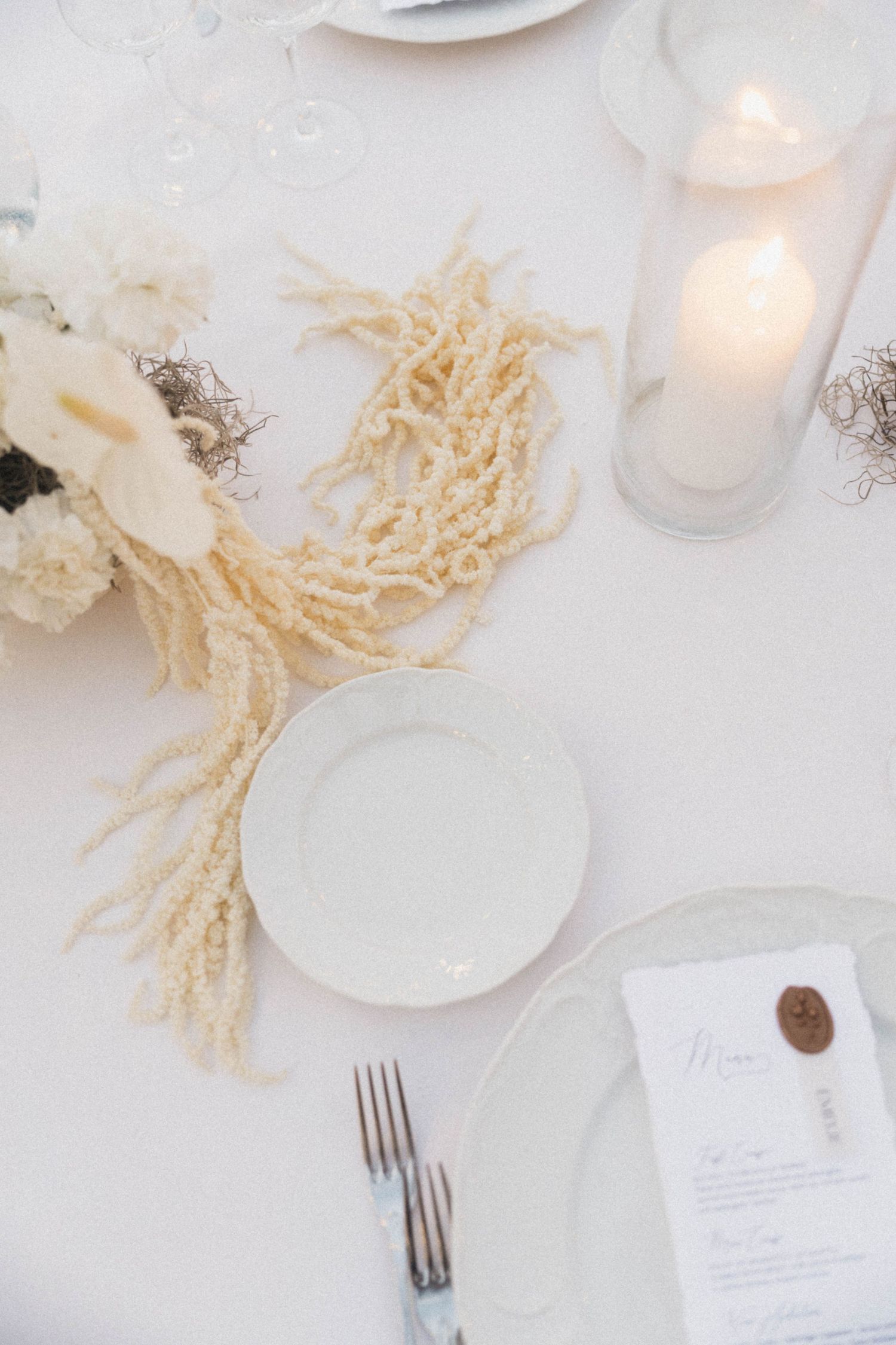 White wedding table setting with coral decor, candle, and wax-sealed menu card.