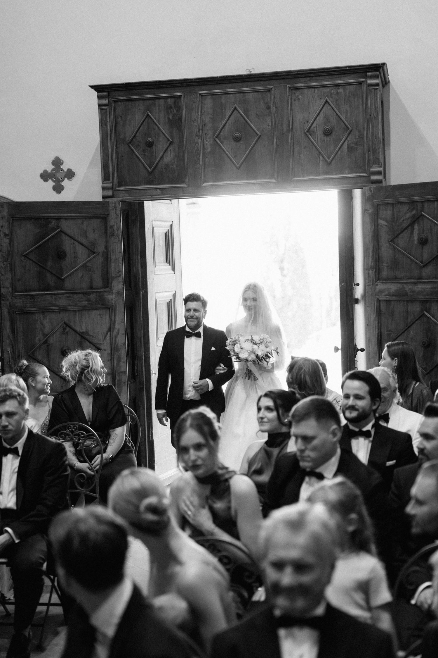 Bride and groom enter church through grand wooden doors as guests turn to watch.
