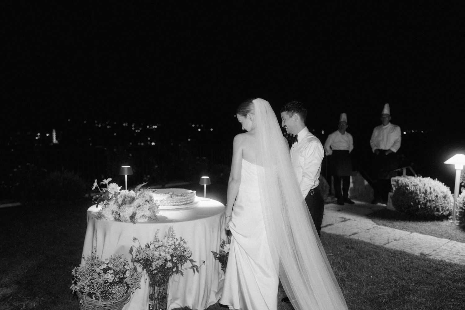 Black and white photo of bride and groom sharing intimate moment outdoors at night with city lights.