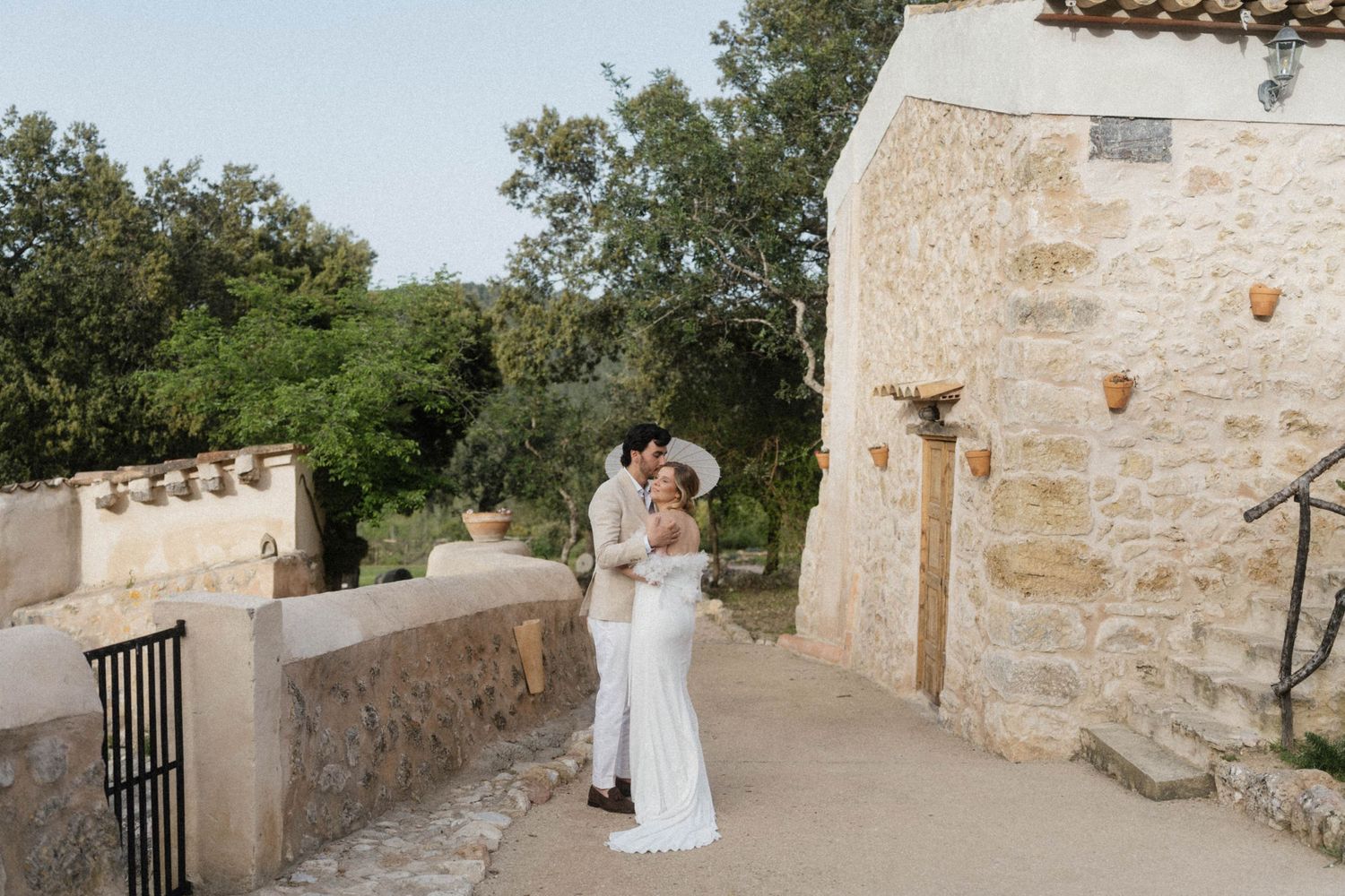 Bride and groom share romantic kiss outside rustic stone building at outdoor wedding venue.