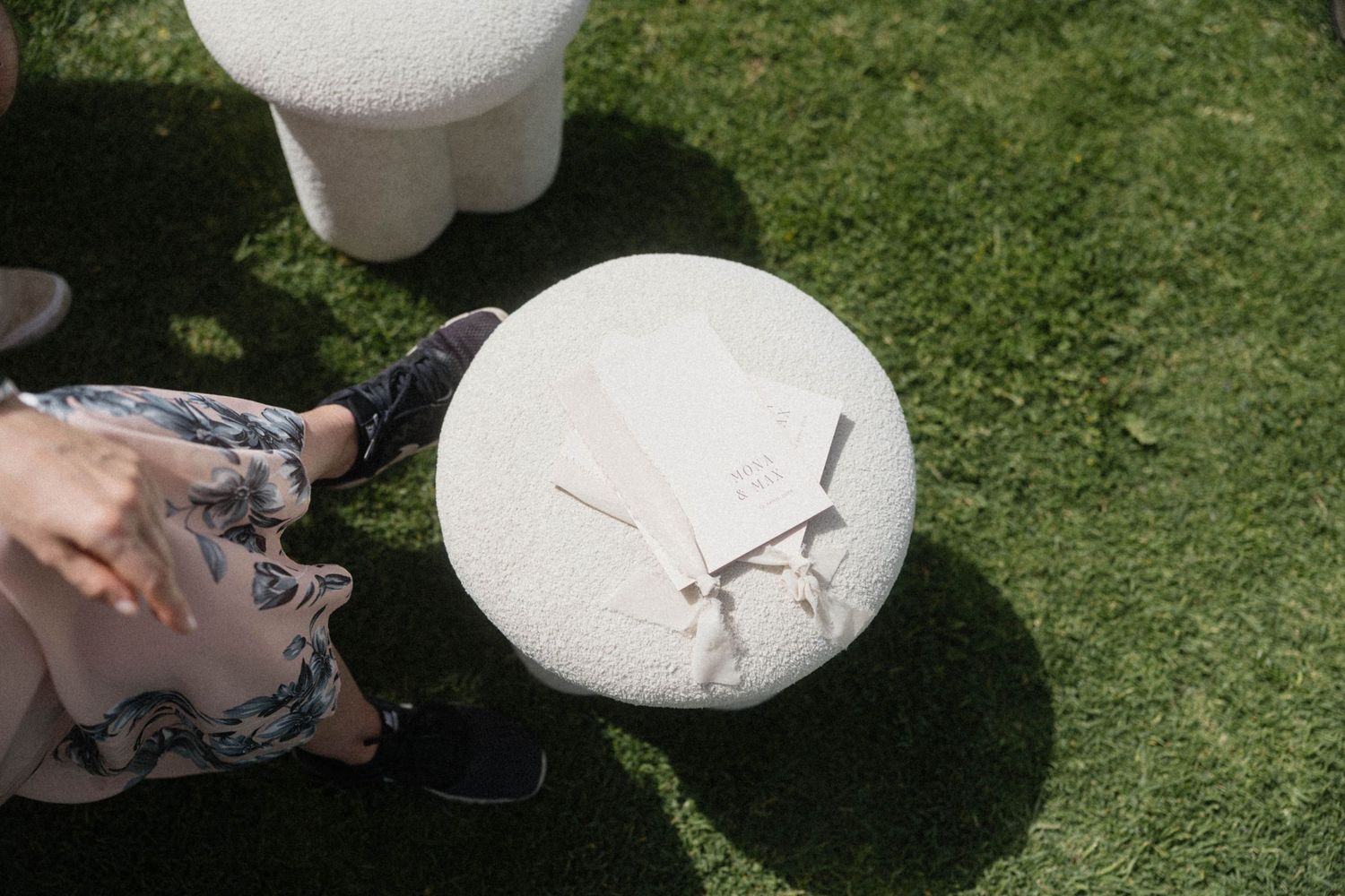 Person pointing at a round stone clock with gold hands resting on green grass at an outdoor wedding.