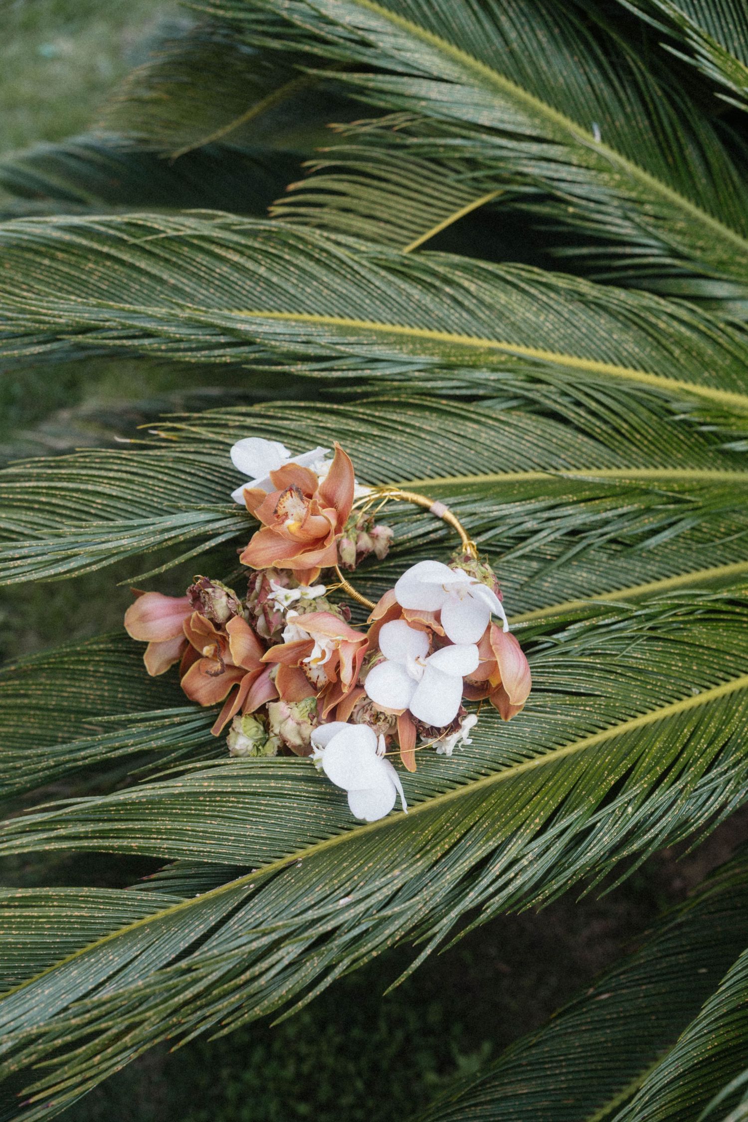 Wedding bouquet with pink and white flowers resting on green tropical palm fronds.