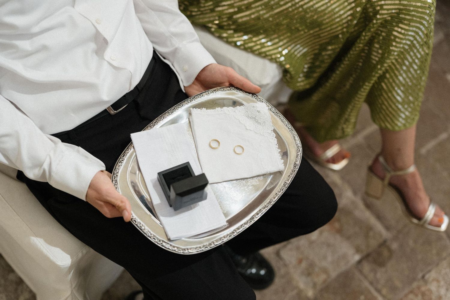 Ring bearer holds a silver tray with wedding rings and a black ring box during a wedding ceremony.